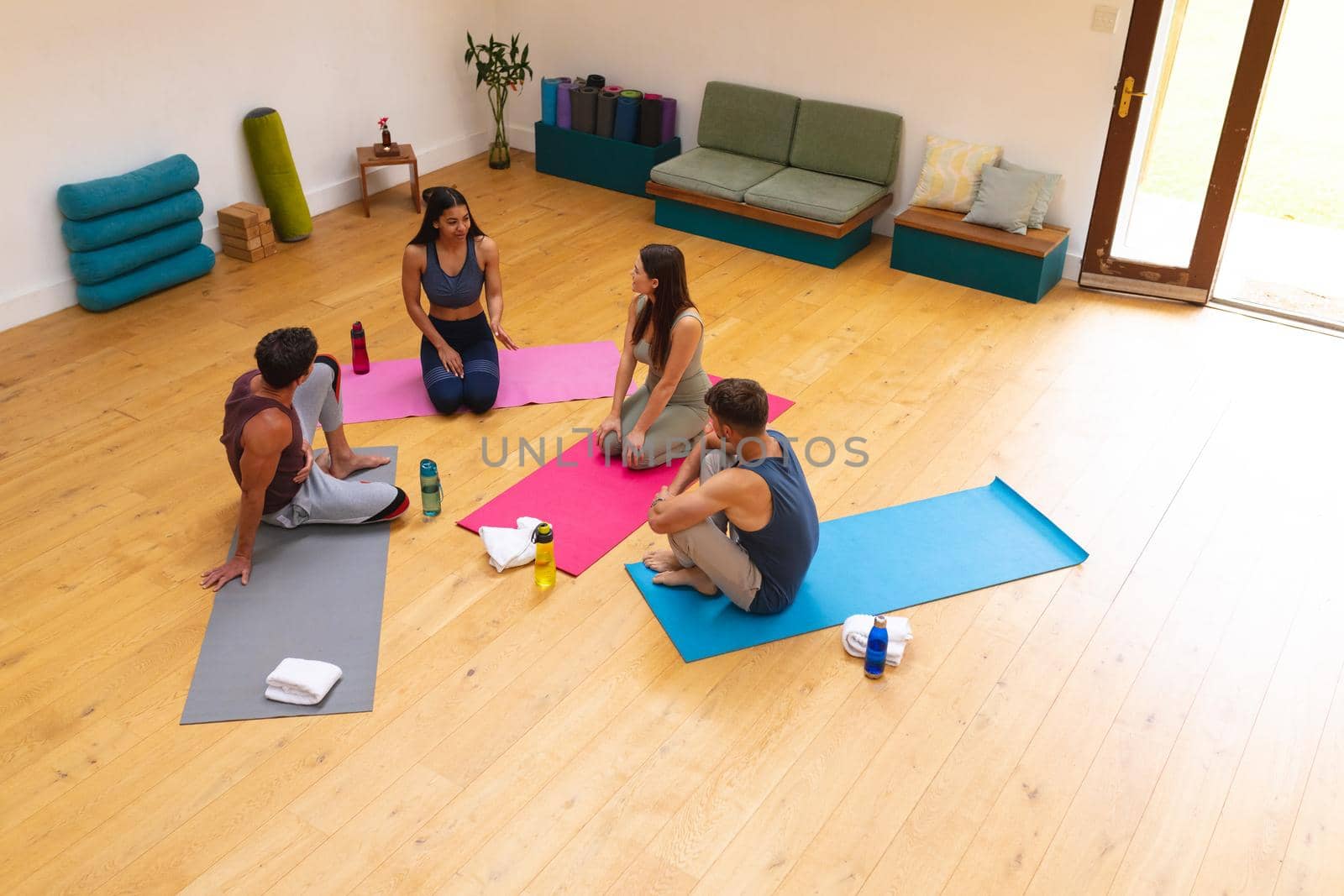 High angle view of multiracial friends discussing while sitting on exercise mats in yoga studio. fitness, yoga and healthy lifestyle.