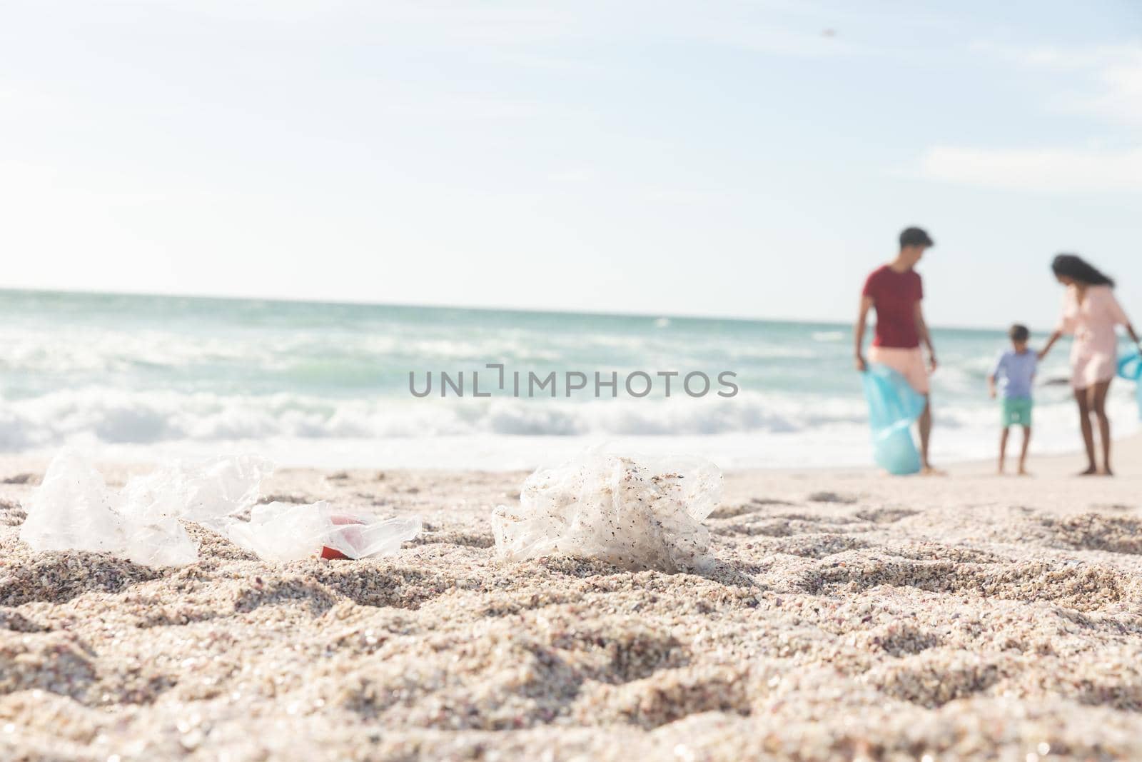 Garbage on sand with multiracial family cleaning beach on sunny day against sky with copy space by Wavebreakmedia