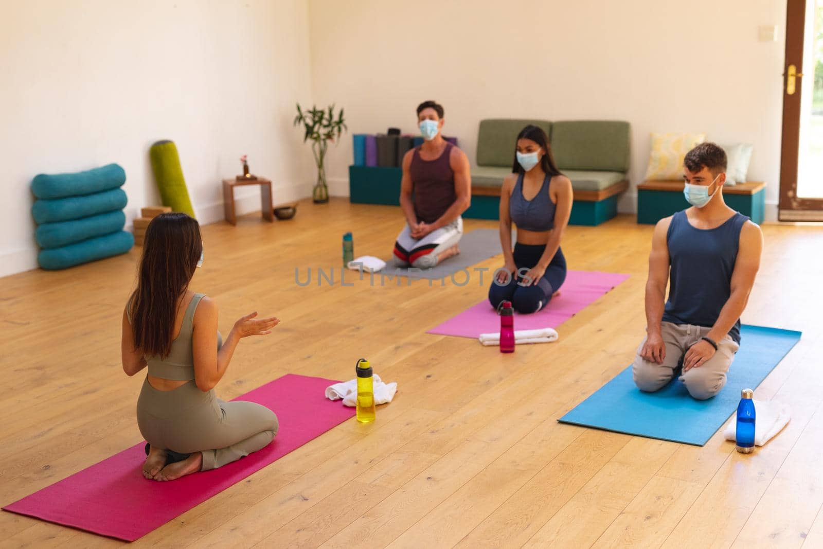 Female instructor with multiracial men and women wearing face masks in yoga studio during covid-19. new normal, illness prevention, pandemic and active lifestyle concept.