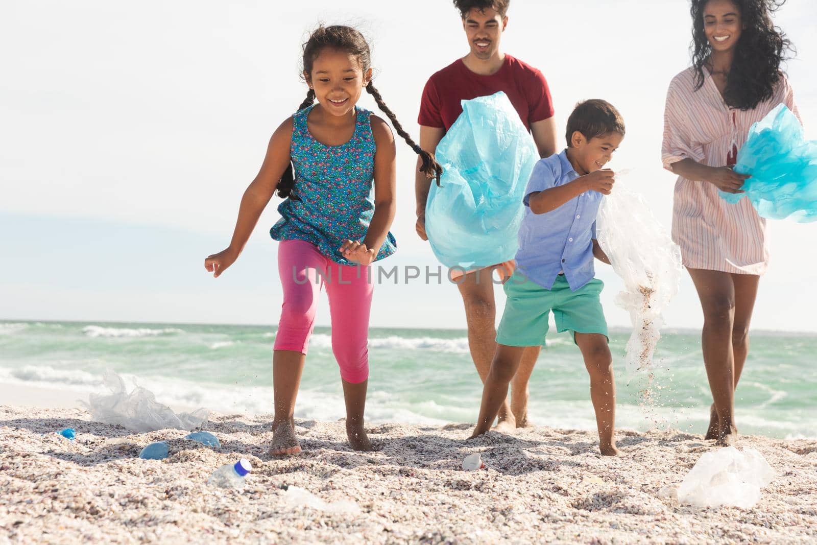 Happy responsible multiracial family collecting plastic garbage from sand at beach on sunny day by Wavebreakmedia
