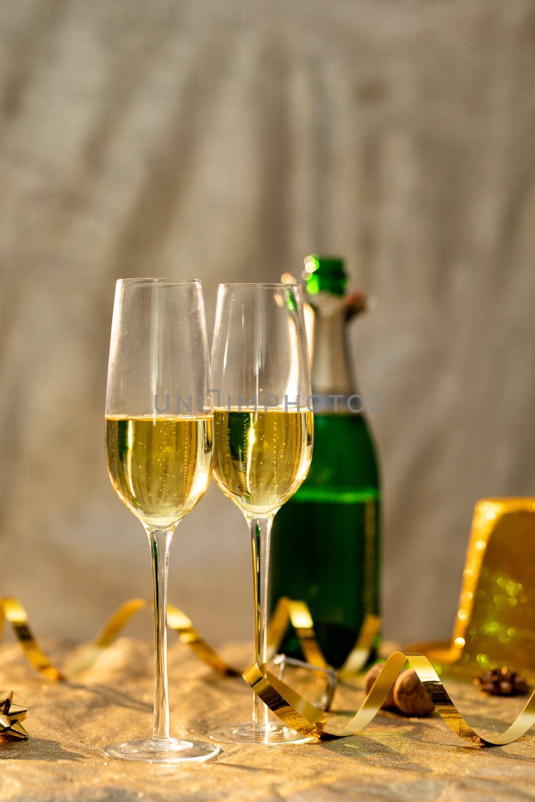 Closeup of champagne flutes by golden ribbon in front of bottle on table. celebration and party with copy space.
