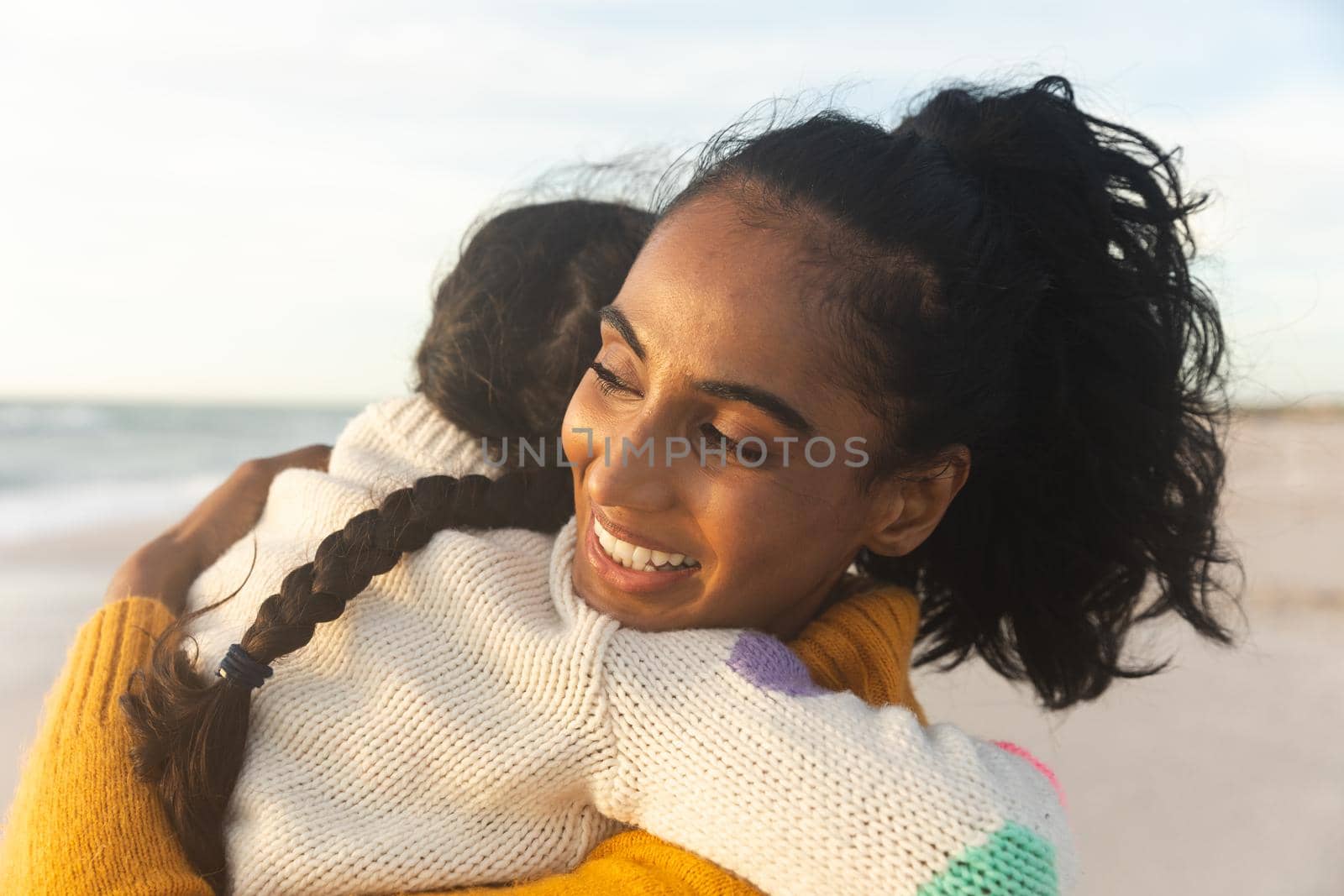 Smiling young biracial woman embracing daughter while carrying her at beach during sunset by Wavebreakmedia