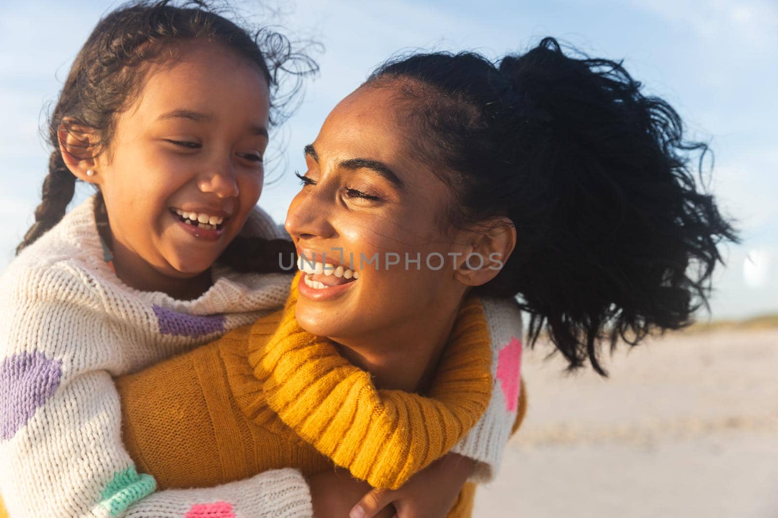 Cheerful young biracial woman looking at daughter while giving her piggyback ride during sunset by Wavebreakmedia