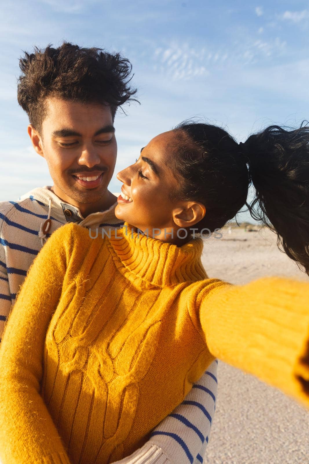 Young biracial woman taking selfie with smiling boyfriend at beach against sky on sunny day by Wavebreakmedia