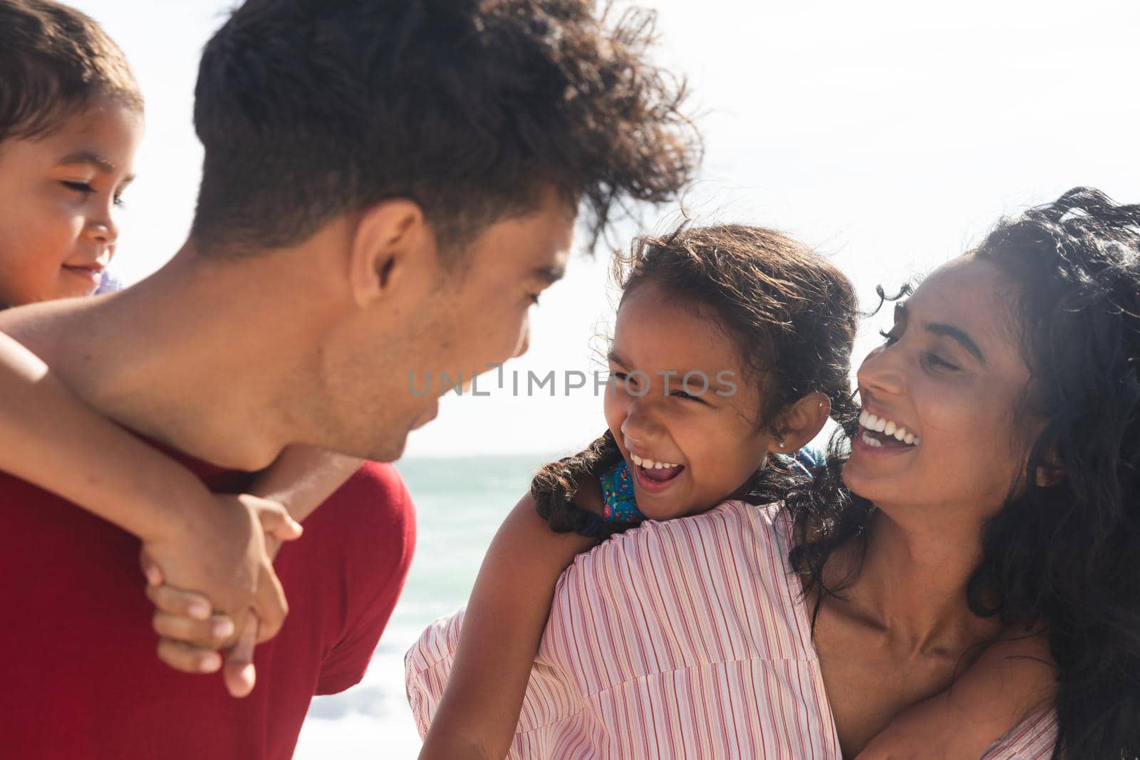 Cheerful multiracial parents giving piggyback rides to children at beach on sunny day by Wavebreakmedia