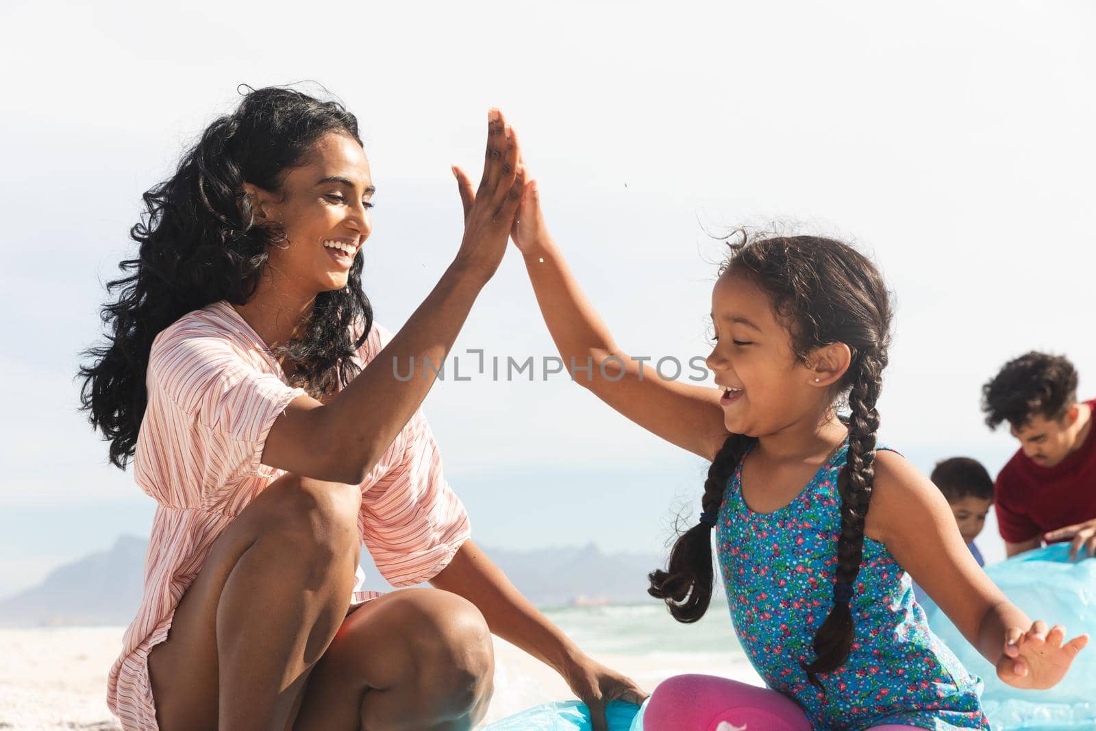 Happy biracial mother and daughter giving high-five while collecting garbage at beach on sunny day. lifestyle and environmentalism.