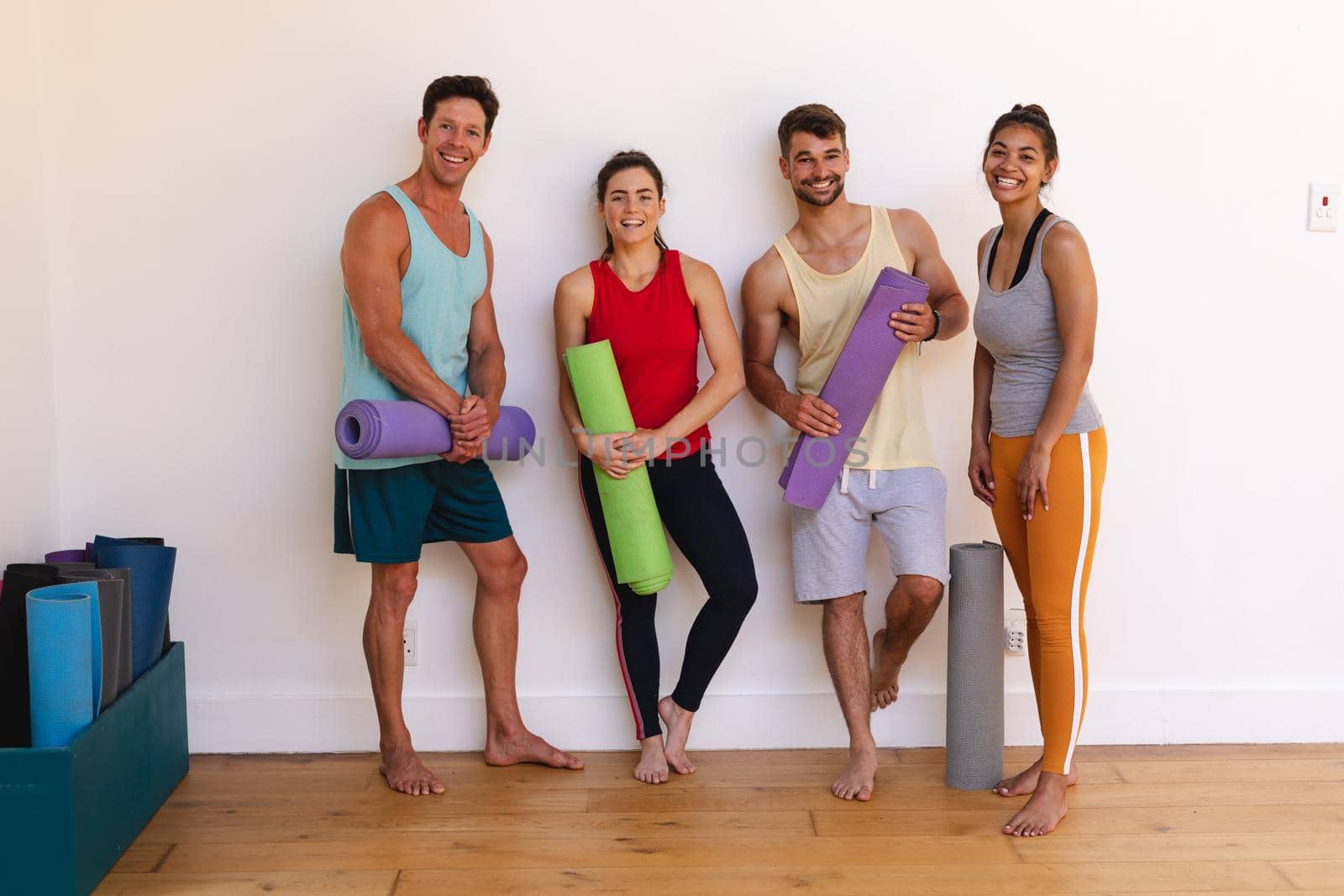 Portrait of smiling multiracial men and women with yoga mats against wall in yoga studio by Wavebreakmedia