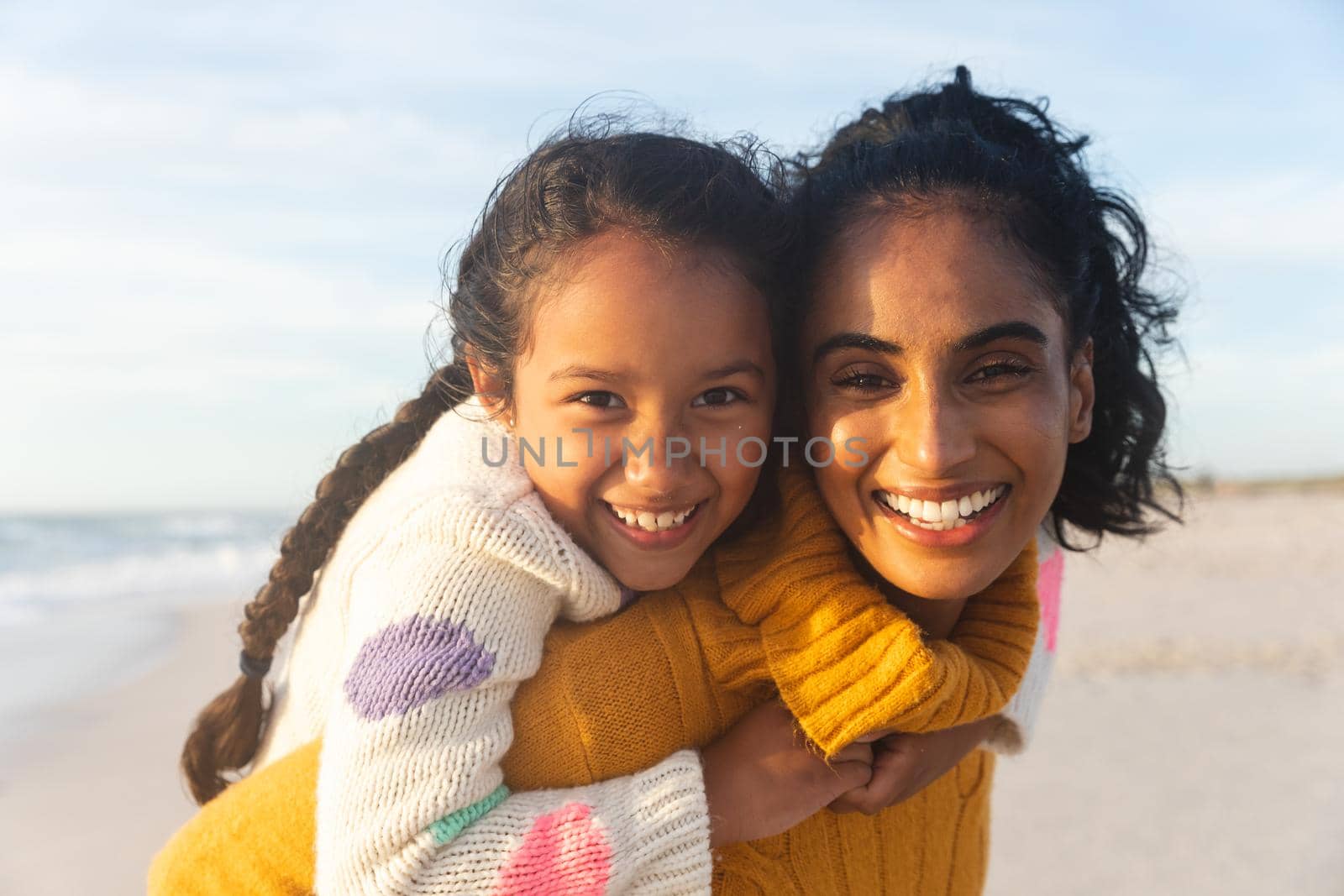 Portrait of happy biracial woman giving piggyback ride to daughter at sunset by Wavebreakmedia