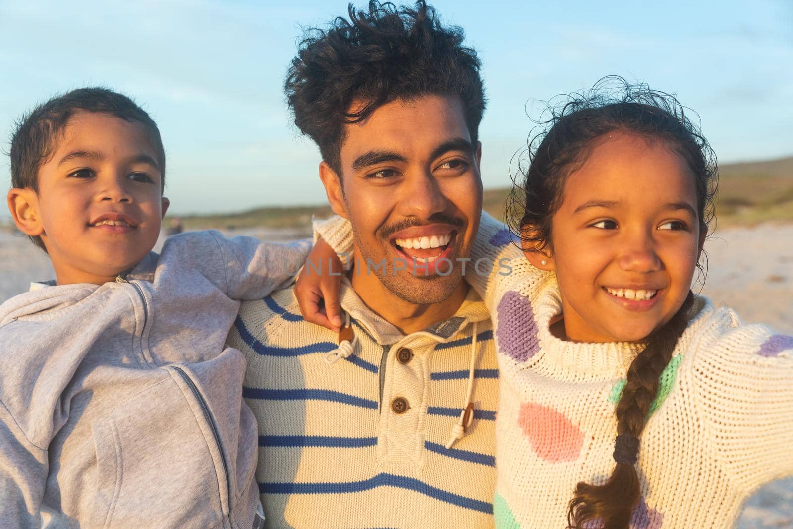 Happy biracial father carrying son and daughter looking away at beach during sunset by Wavebreakmedia
