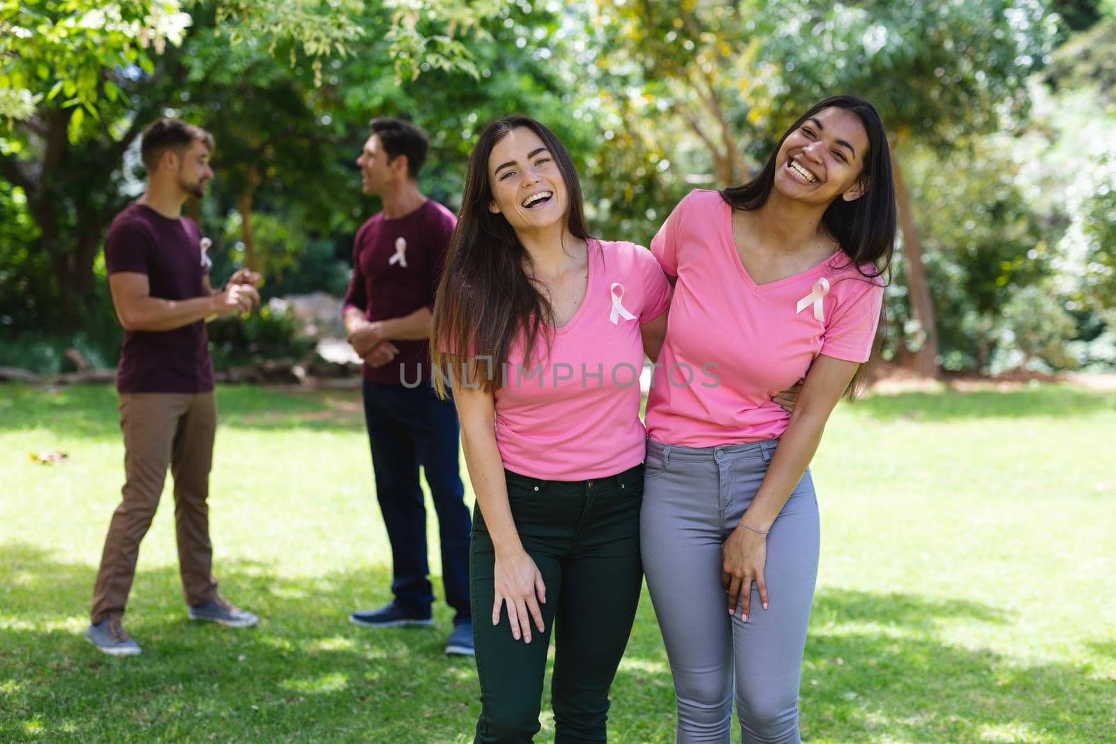 Portrait of happy multiracial female friends wearing breast cancer awareness ribbons at park by Wavebreakmedia