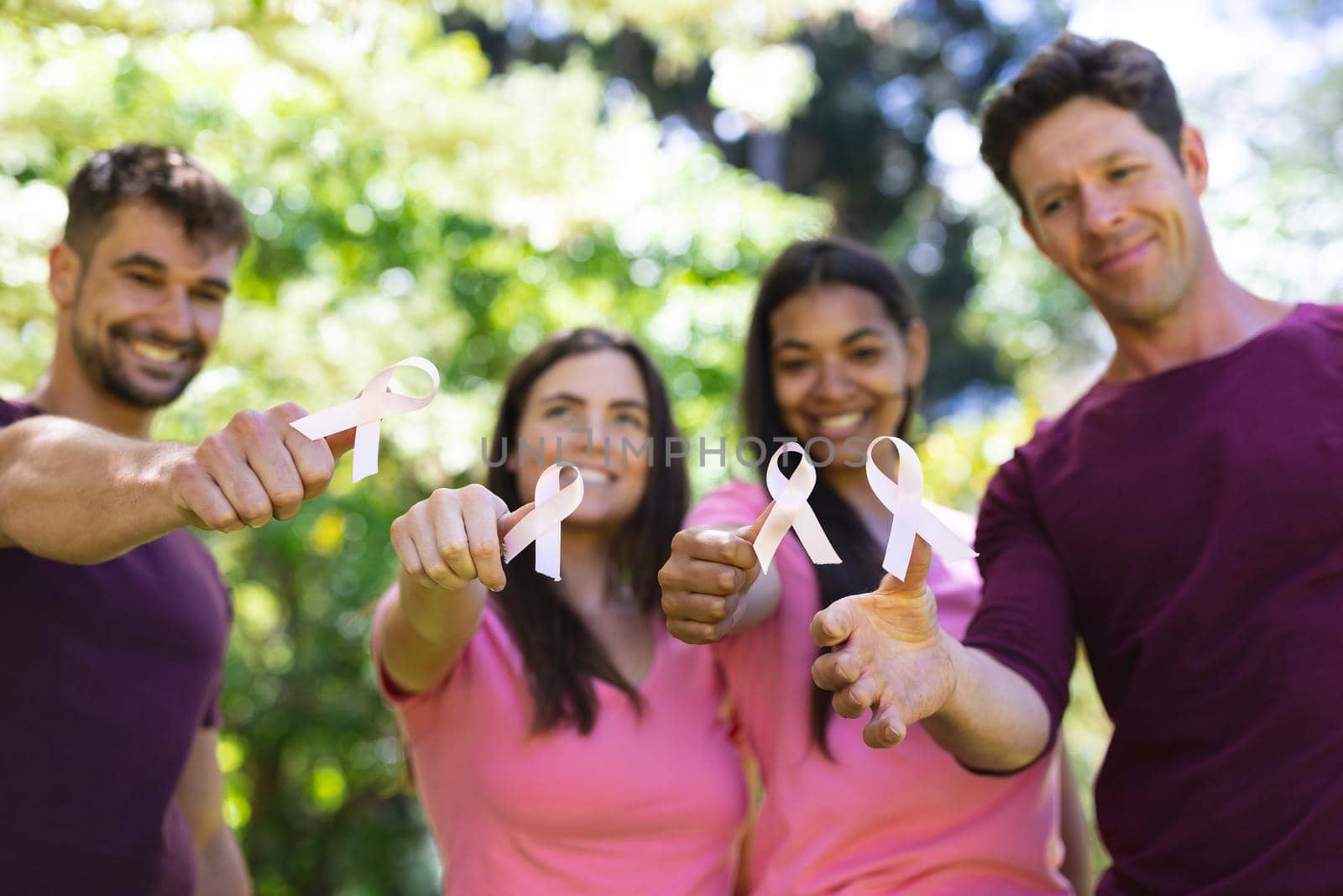 Portrait of smiling multiracial men and women showing breast cancer awareness ribbons in park. breast cancer awareness campaign, friendship and unity concept.