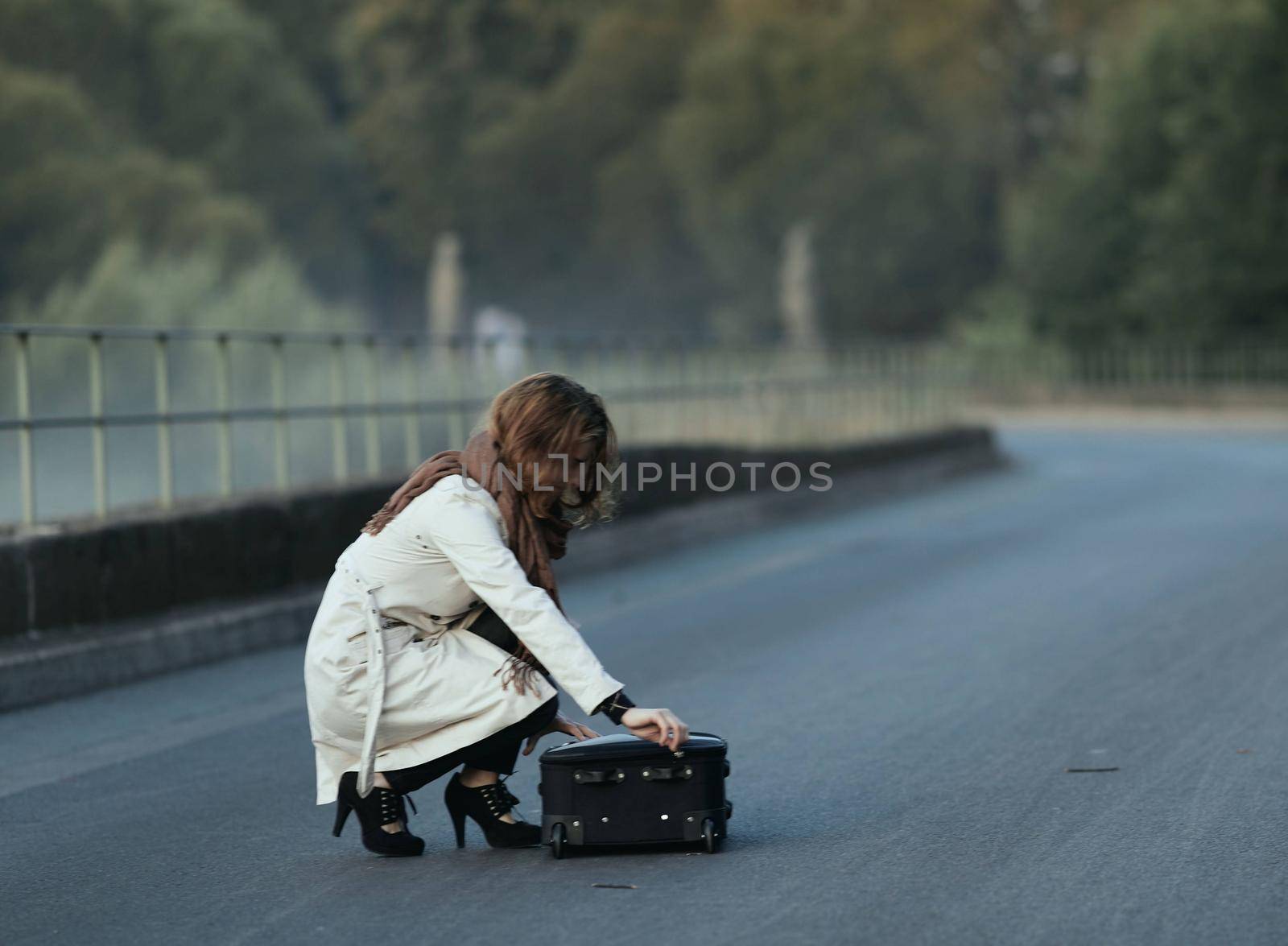 dramatic moment in life of breakup of a relationship with a once loved one fleeing with one suitcase in the photo, the girl collects things in a suitcase in the middle of the roadway by Costin