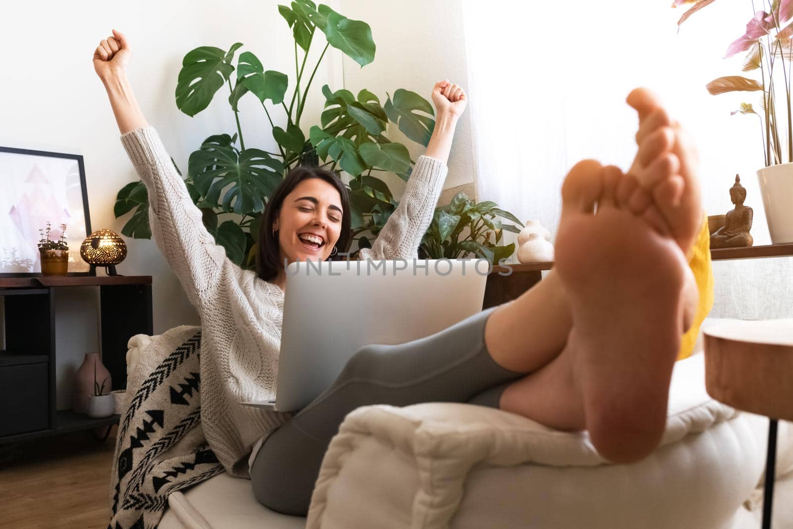 Excited and happy young caucasian woman raising arms up celebrating success or achievement at home using laptop by Hoverstock