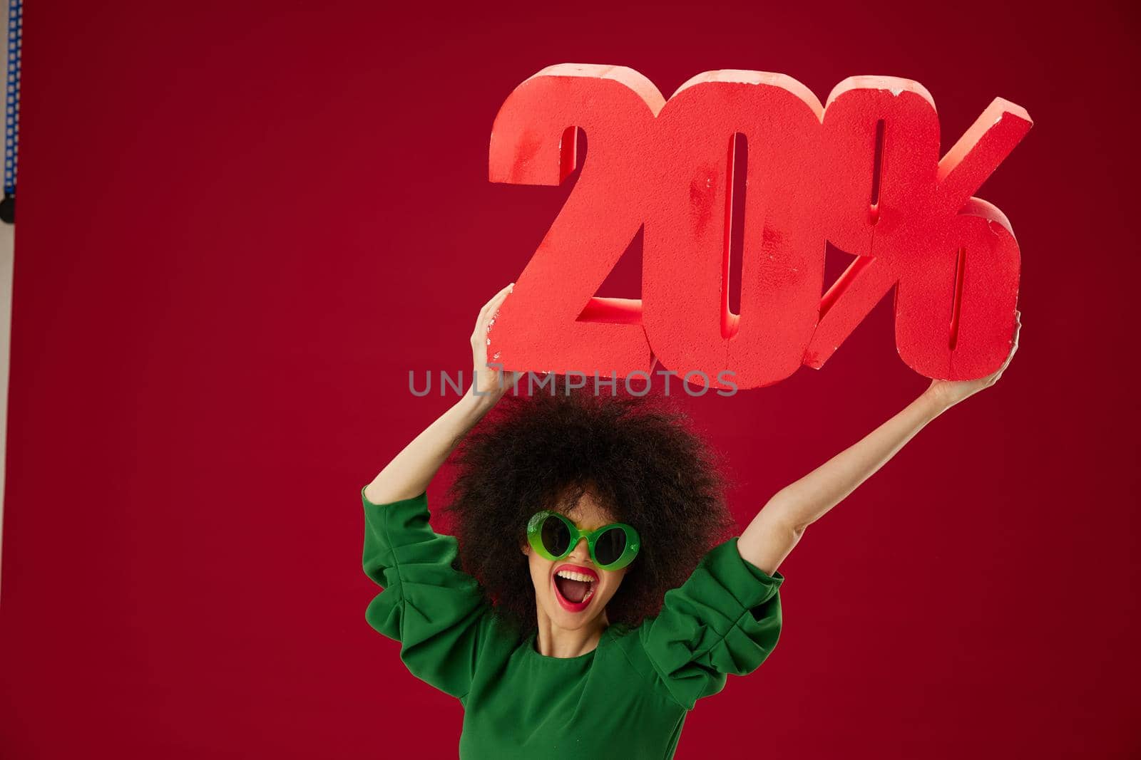 Portrait of a charming lady green dress afro hairstyle dark glasses twenty percent in hands red background unaltered by SHOTPRIME
