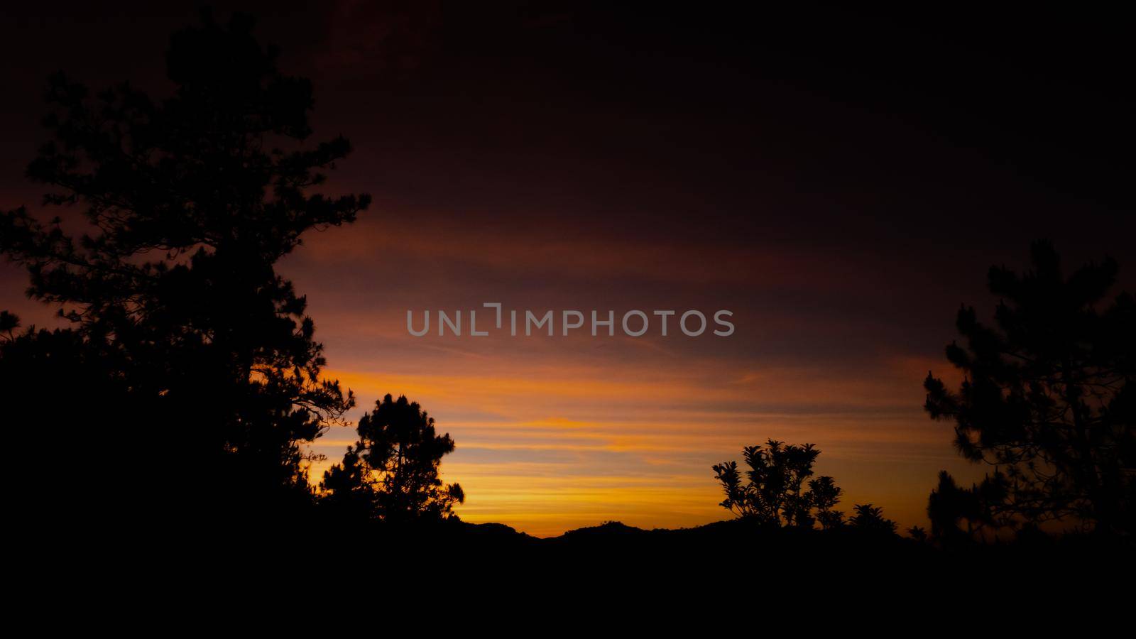 Beautiful landscape silhouette on the mountain peak during sunset with warm sunlight and dramatic sky. by TEERASAK