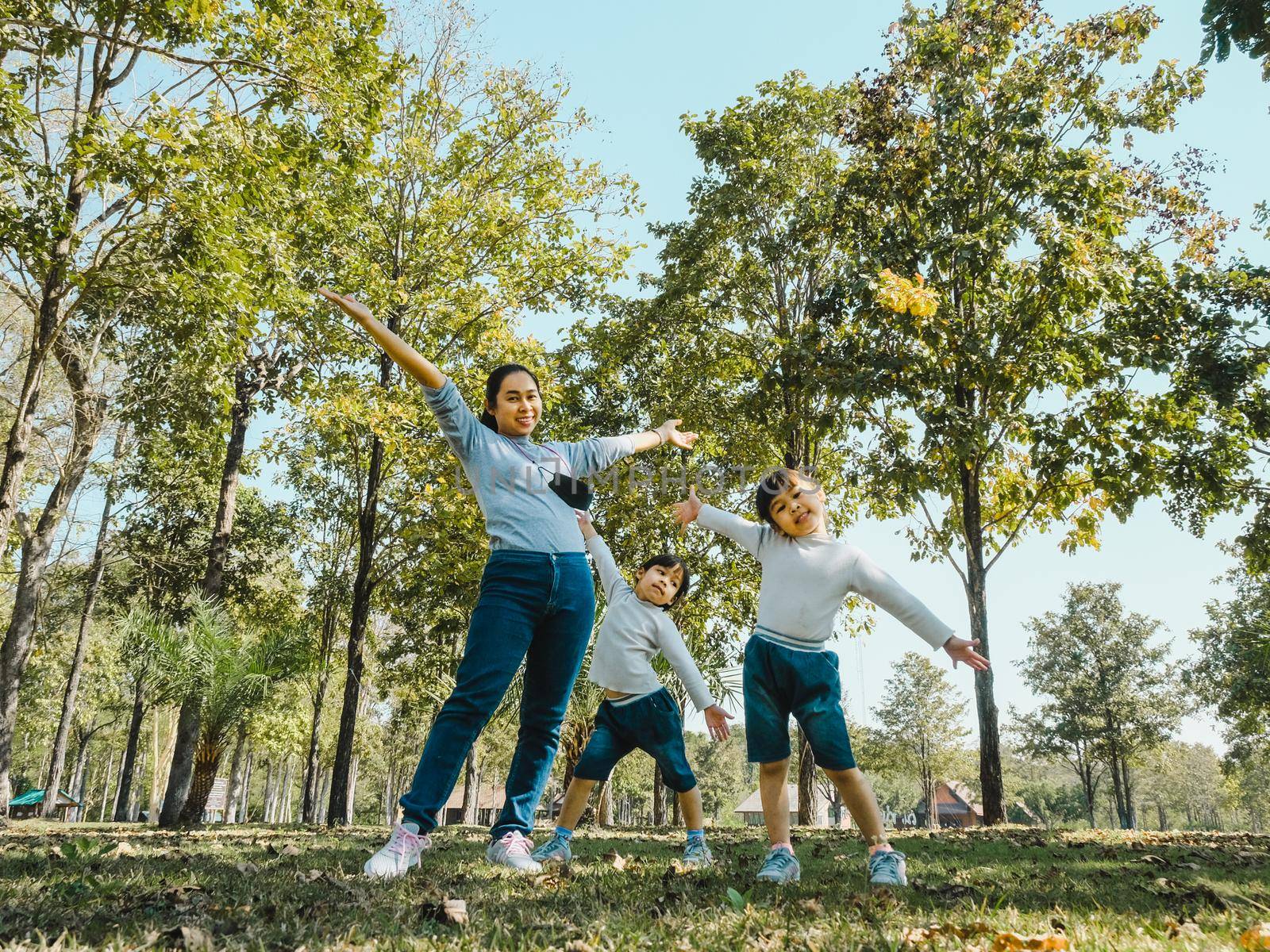 Two cute little Asian girls in summer outfits, having fun with a beautiful young mother smiling happily in the park. Motherhood and family concept. by TEERASAK