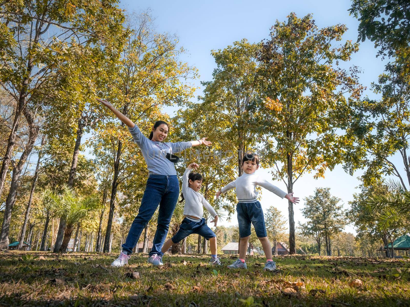 Two cute little Asian girls in summer outfits, having fun with a beautiful young mother smiling happily in the park. Motherhood and family concept. by TEERASAK