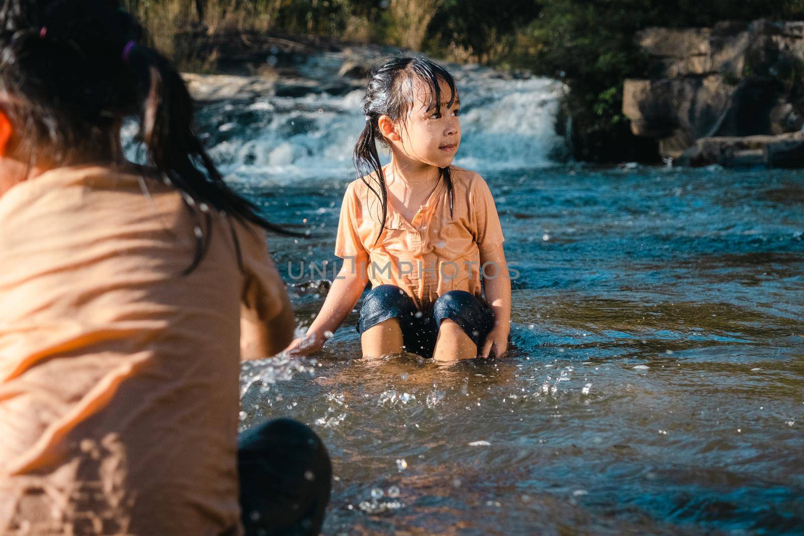 Asian little girl playing in the forest stream with her sister. Active recreation with children on river in summer. by TEERASAK