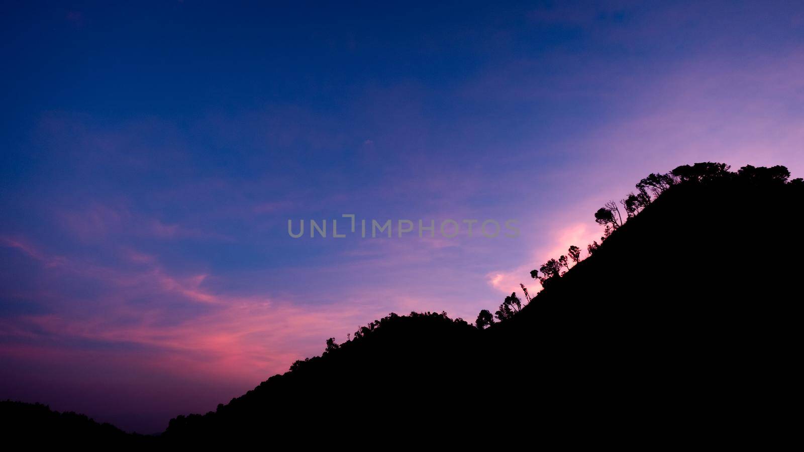 Beautiful landscape silhouette on the mountain peak during sunset with warm sunlight and dramatic sky. by TEERASAK