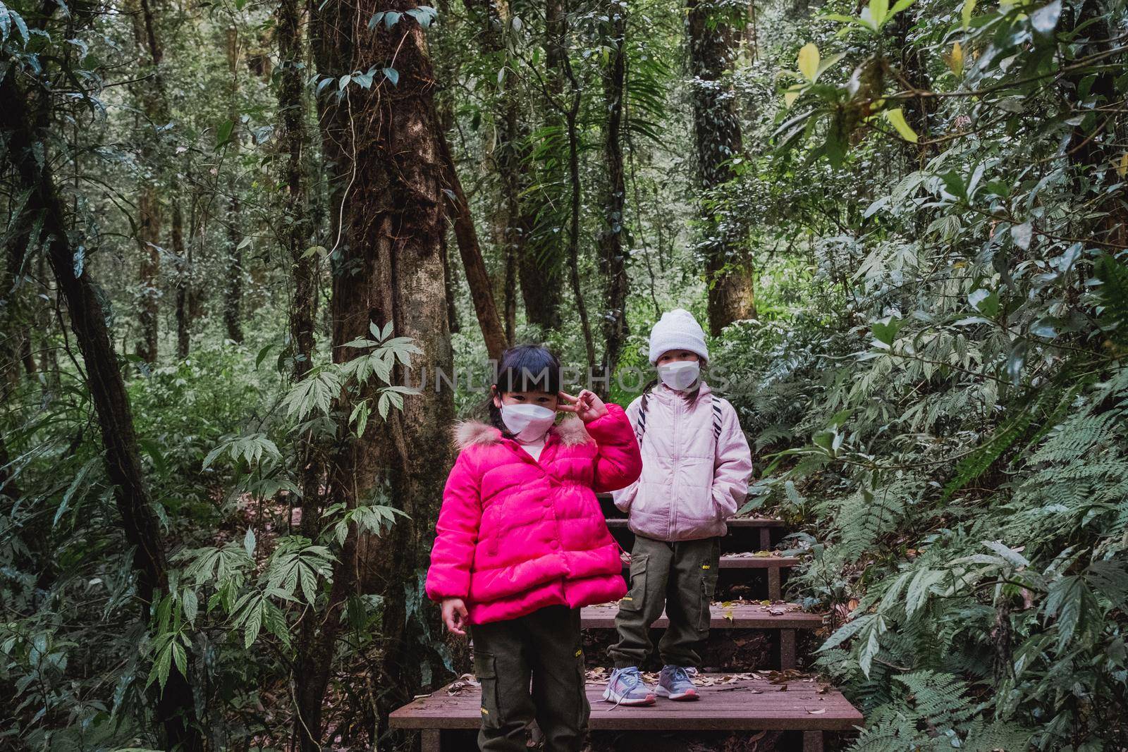 Children with backpacks hiking in nature with family. Two preschoolers in winter clothes explore the forest, play and learn in nature. a new normal lifestyle. by TEERASAK