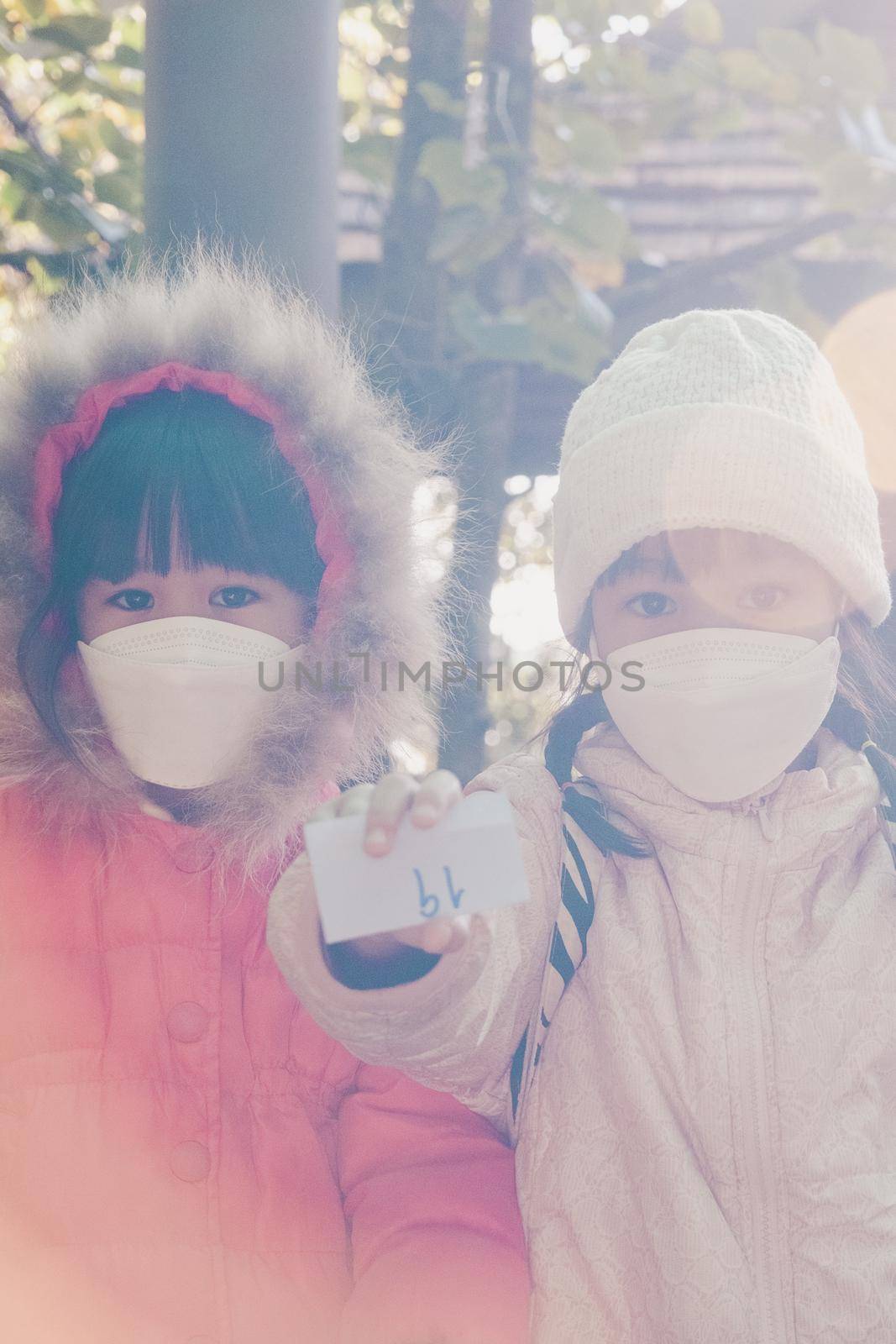 Children in protective face mask and winter clothes sit and wait to prepare for the hiking in nature with family. Learning activities and exploring nature on vacation. a new normal lifestyle. by TEERASAK