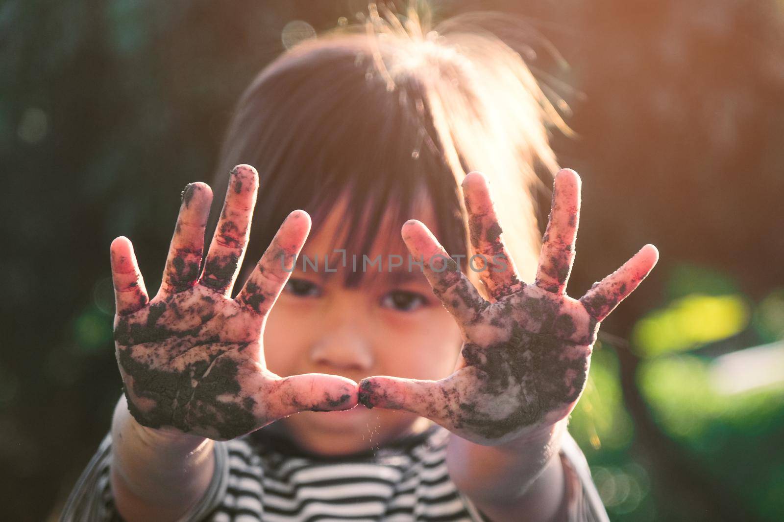 Cute little girl smiles and shows off her muddy hands while planting trees in the backyard. Educational concept outside the school fence.