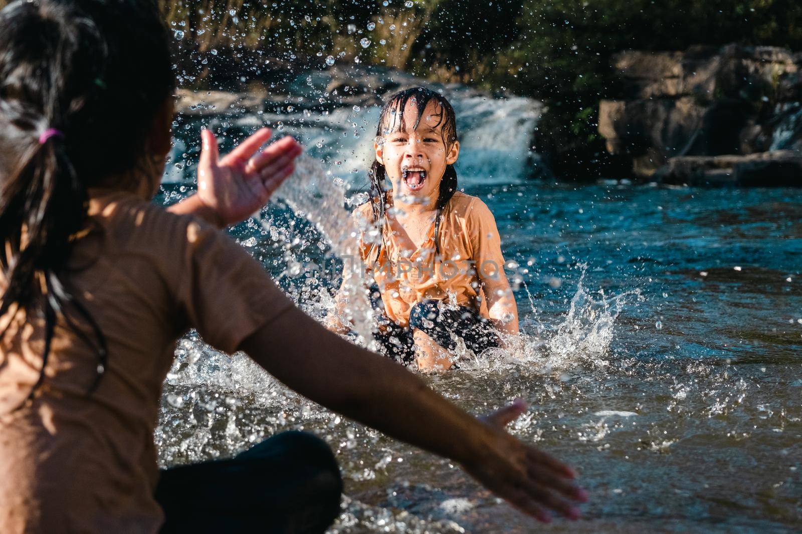 Asian little girl playing in the forest stream with her sister. Active recreation with children on river in summer. by TEERASAK