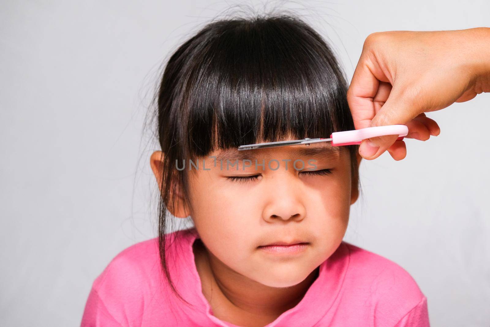Asian mother cuts her daughter's hair by herself at home. Mom cuts hair for a cute little girl. Stay home safe from corona virus Covid-19 by TEERASAK