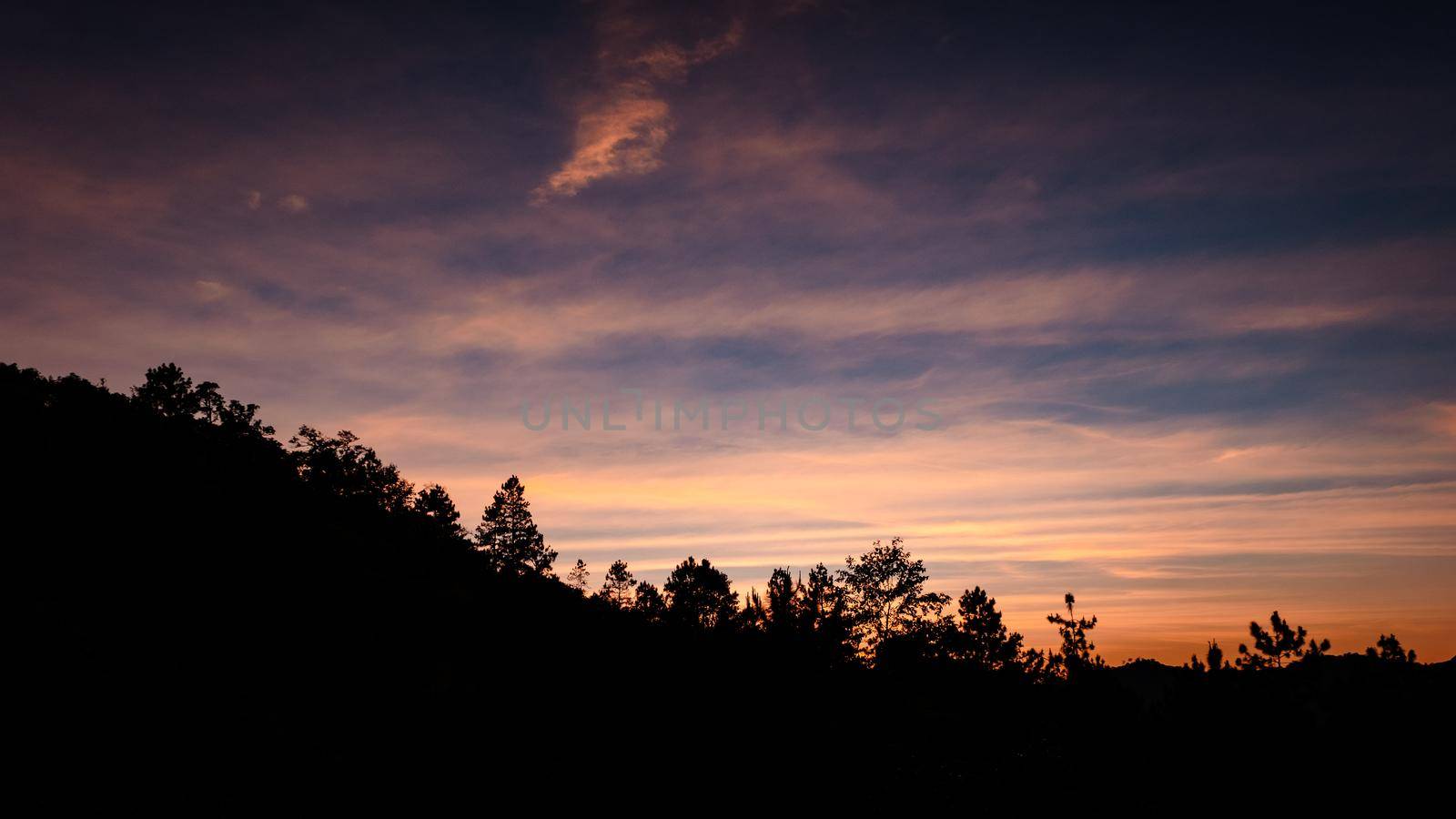 Beautiful landscape silhouette on the mountain peak during sunset with warm sunlight and dramatic sky. by TEERASAK