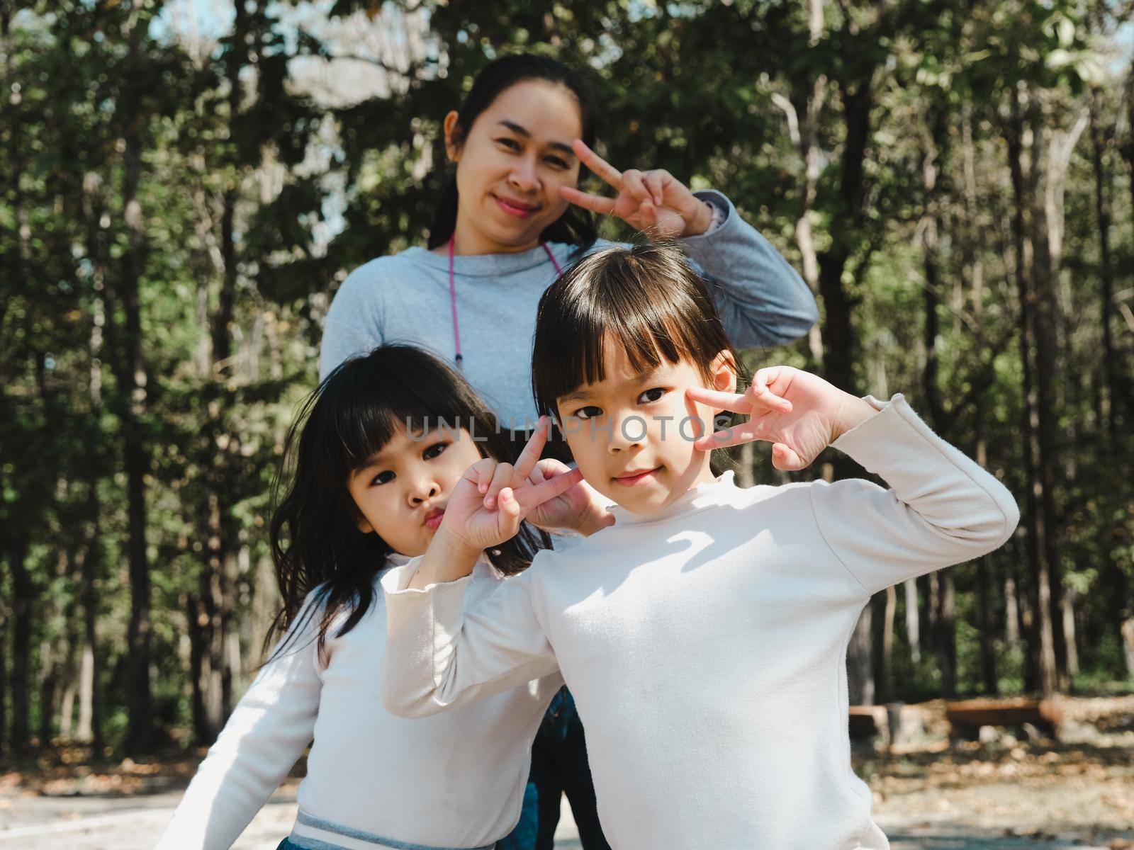Two cute little Asian girls in summer outfits, having fun with a beautiful young mother smiling happily in the park. Motherhood and family concept.