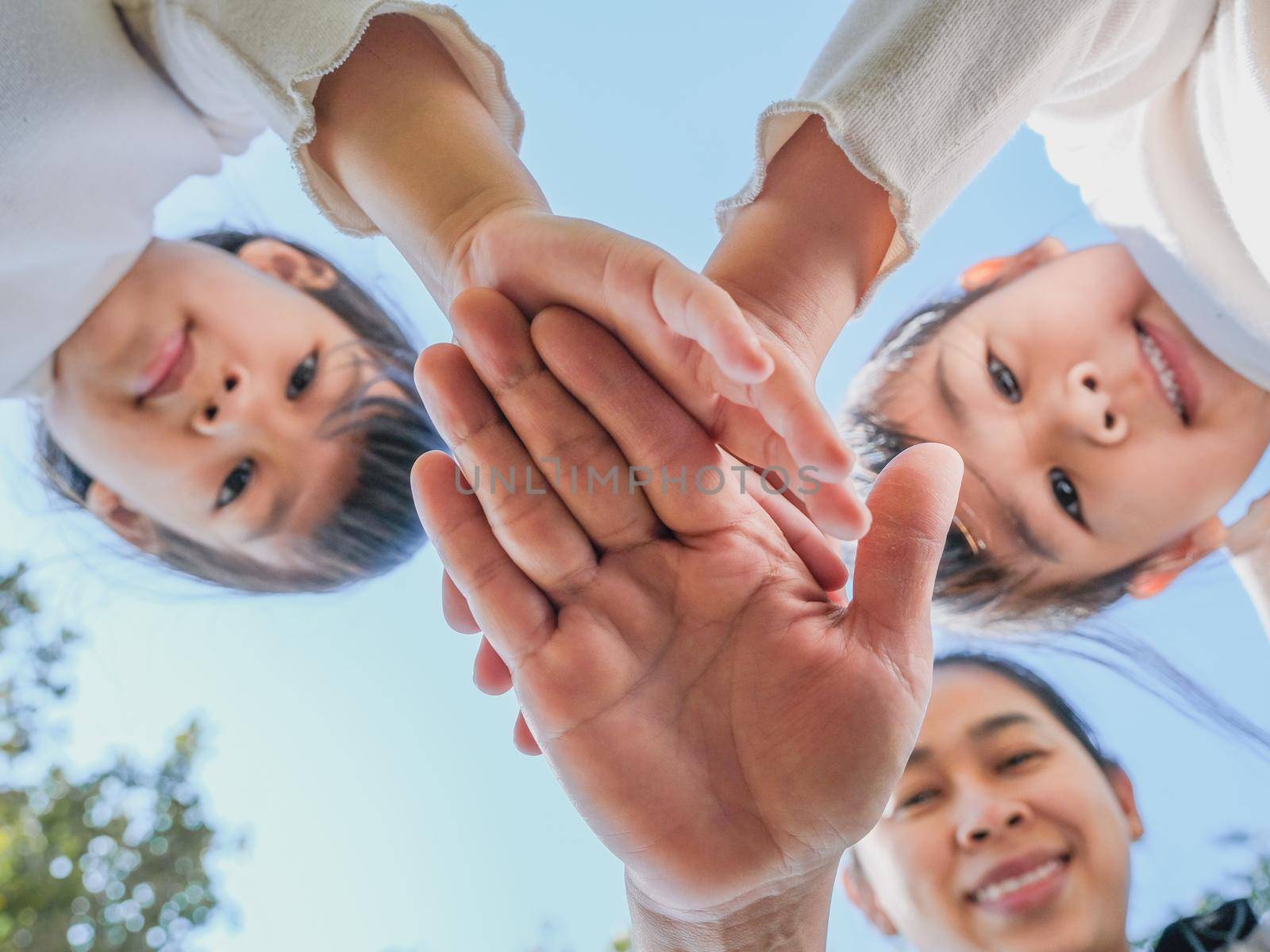 Close up of family hands put their hands together against blue sky  background on a warm sunny day. Happy people or team participation.