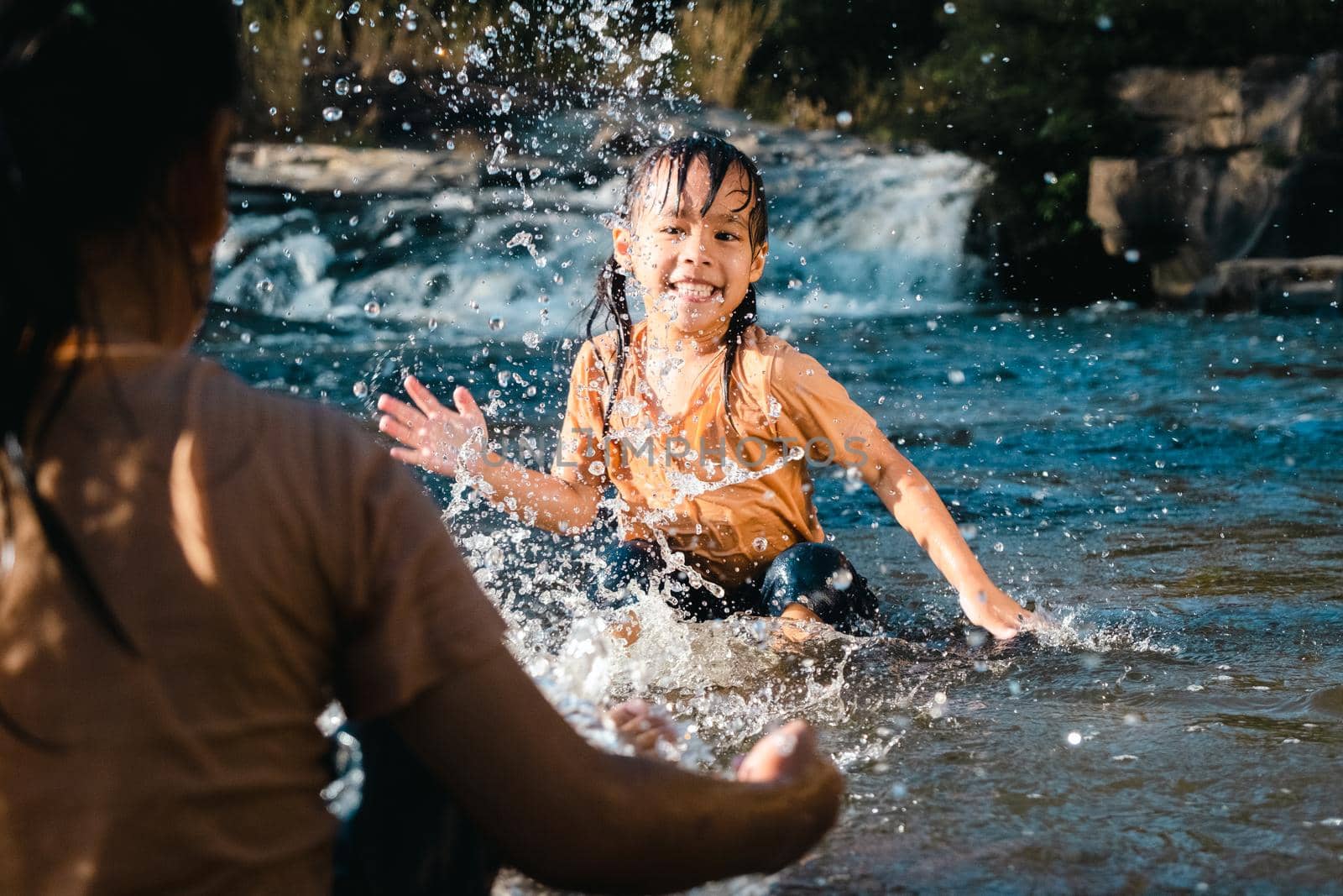 Asian little girl playing in the forest stream with her sister. Active recreation with children on river in summer.