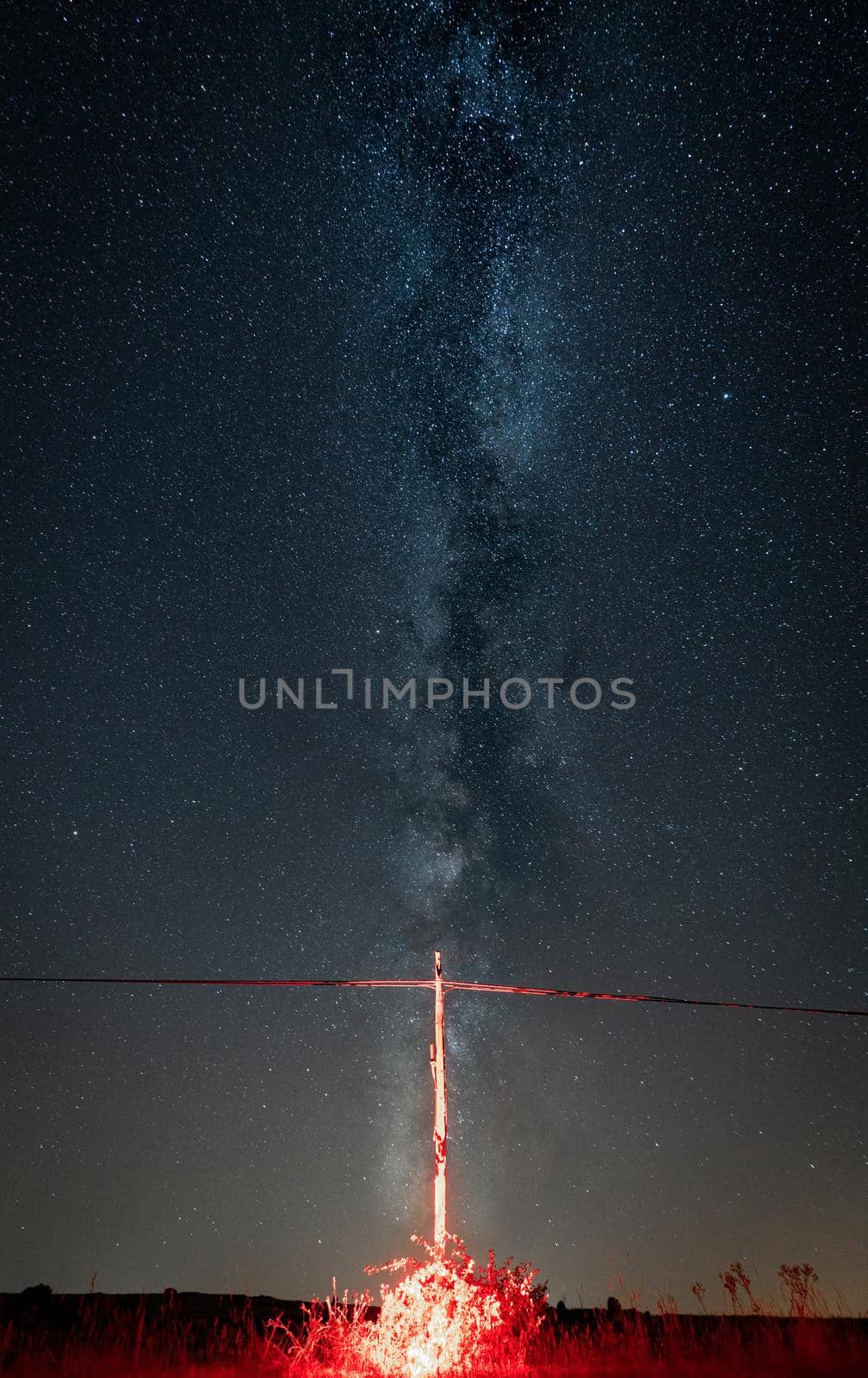 Spectacular power line and wooden pylon in bright red under milky way by FerradalFCG