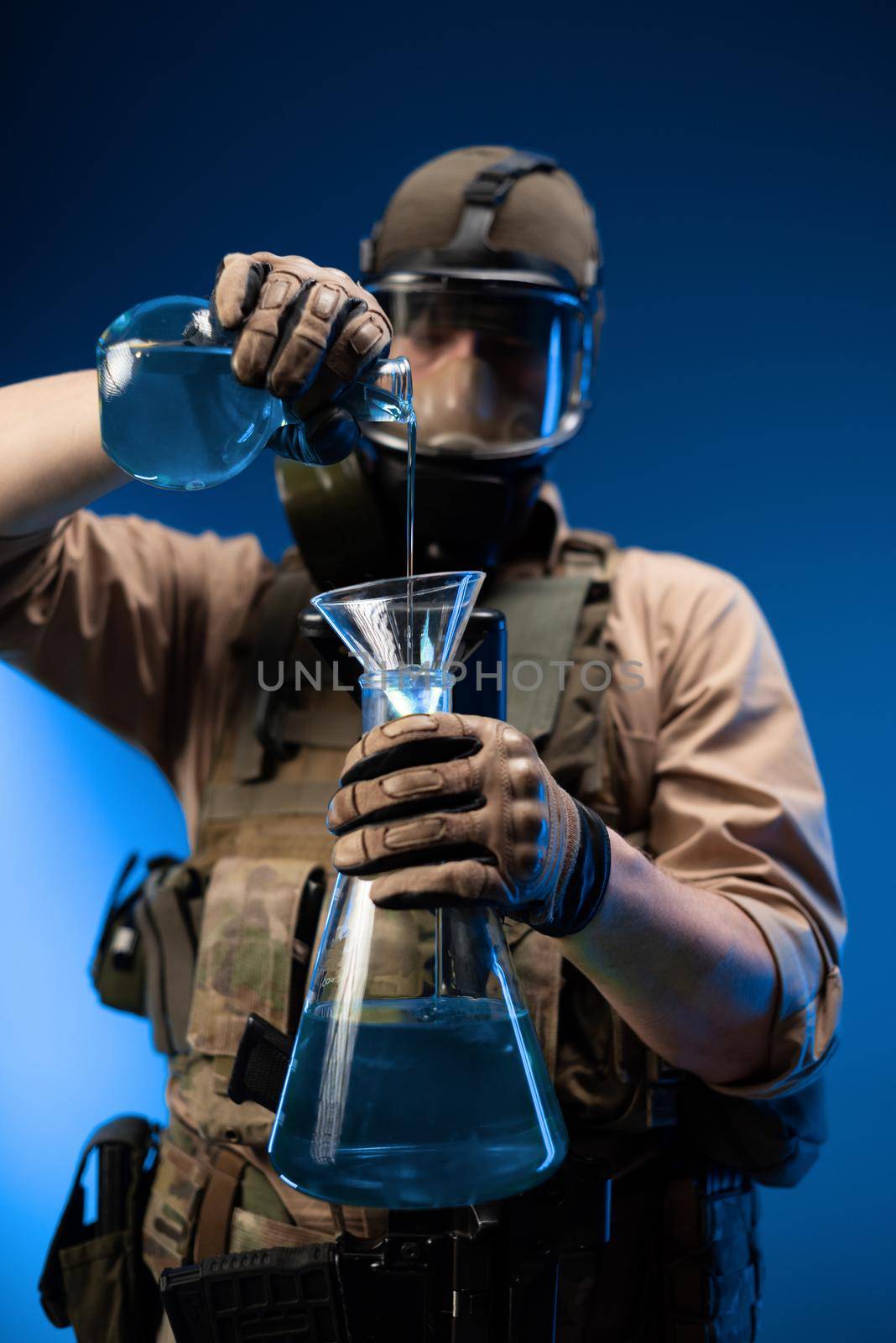 a man in military clothes and a gas mask with laboratory chemical flasks pours reagents by Rotozey