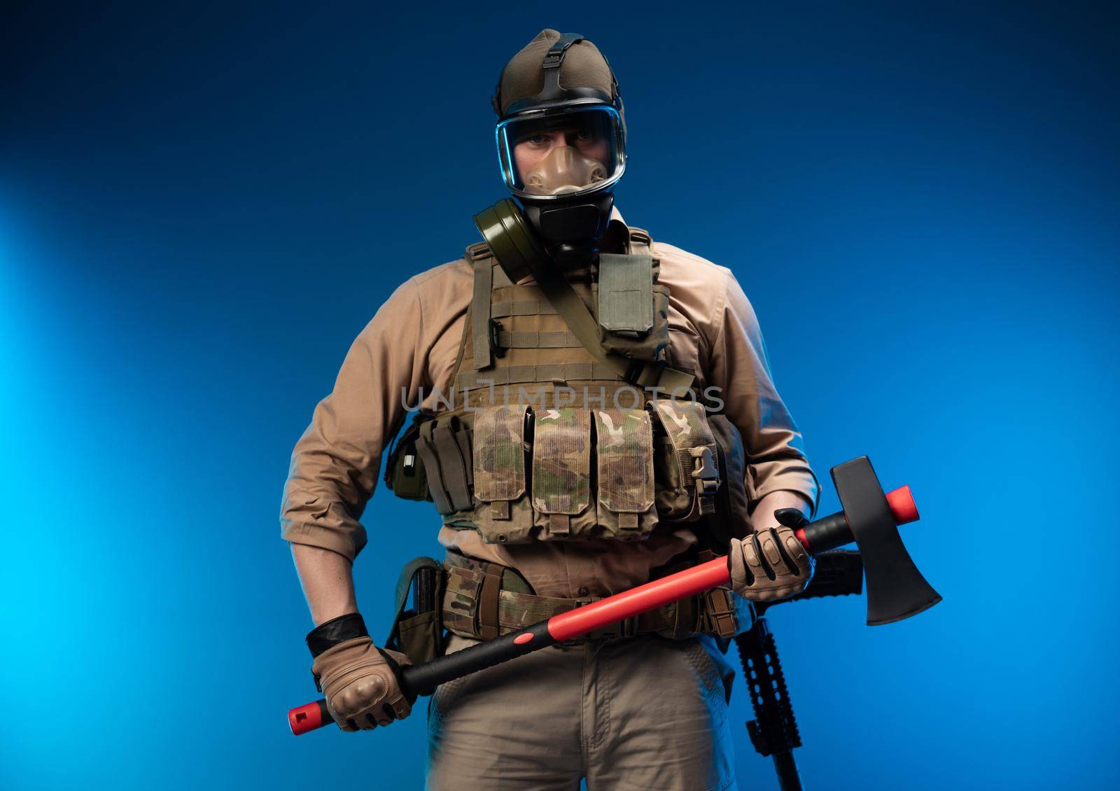 a soldier in military clothes with a bulletproof vest in a gas mask holds a red fire axe in his hands by Rotozey