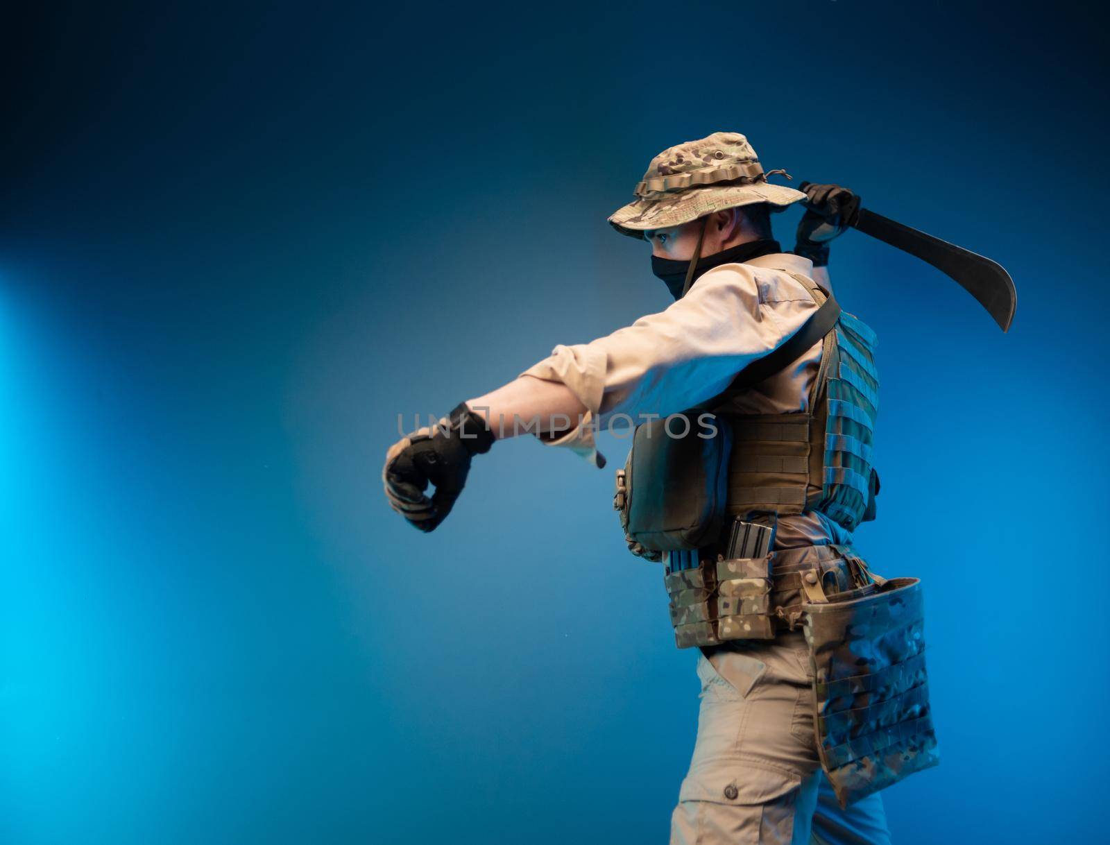 an army soldier in military clothes swings to strike with a machete in his hand by Rotozey