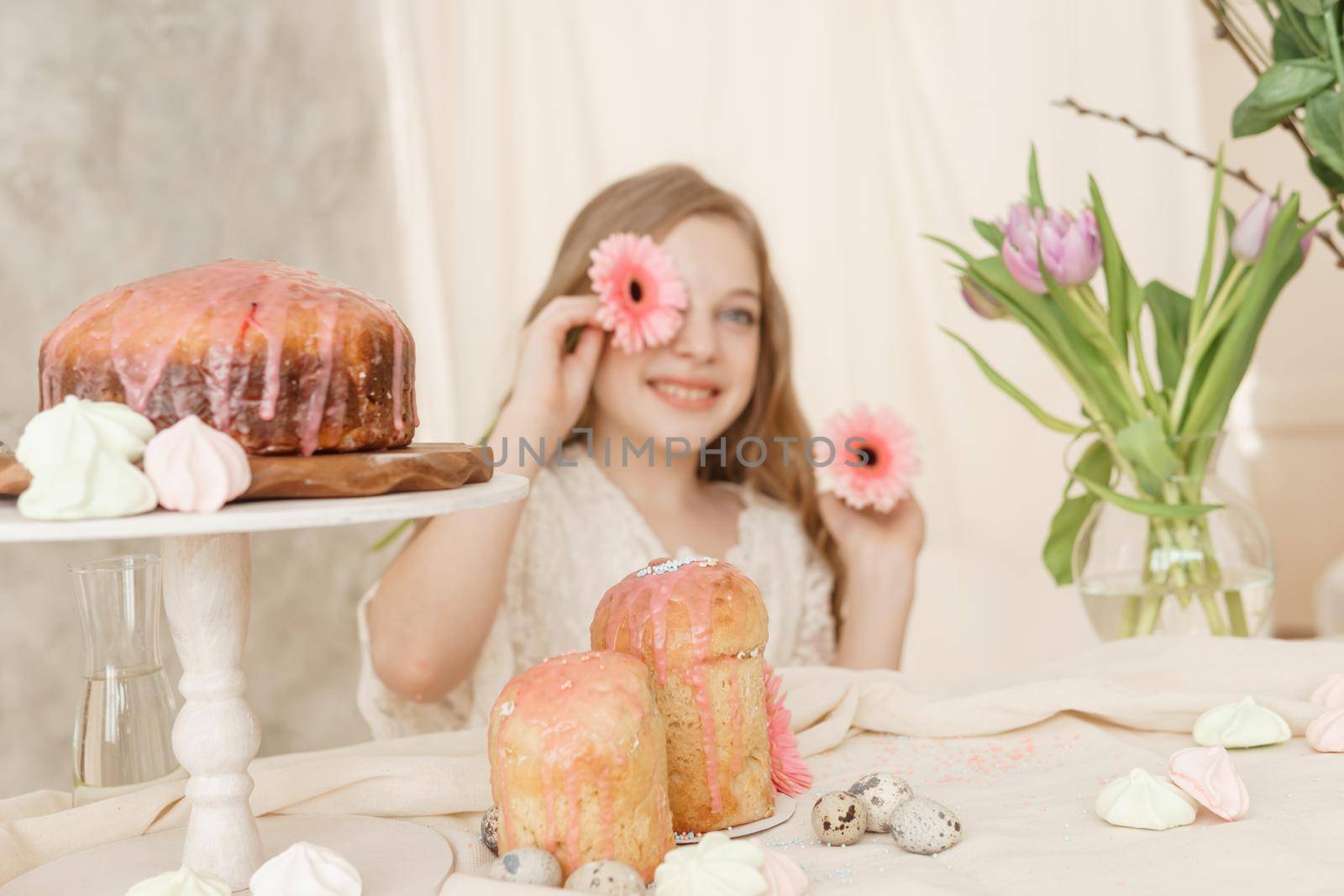 A girl with long hair in a light dress is sitting at the Easter table with cakes, spring flowers and quail eggs. Happy Easter celebration