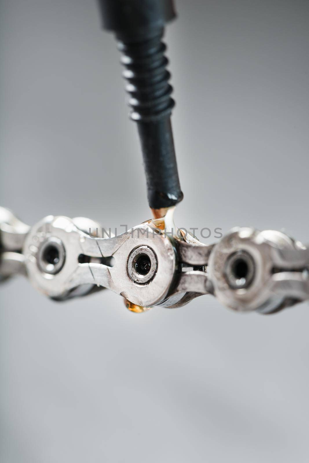 Greasing a bicycle chain with a drop of golden oil close-up on a gray background. Taking care of the bike drive system.
