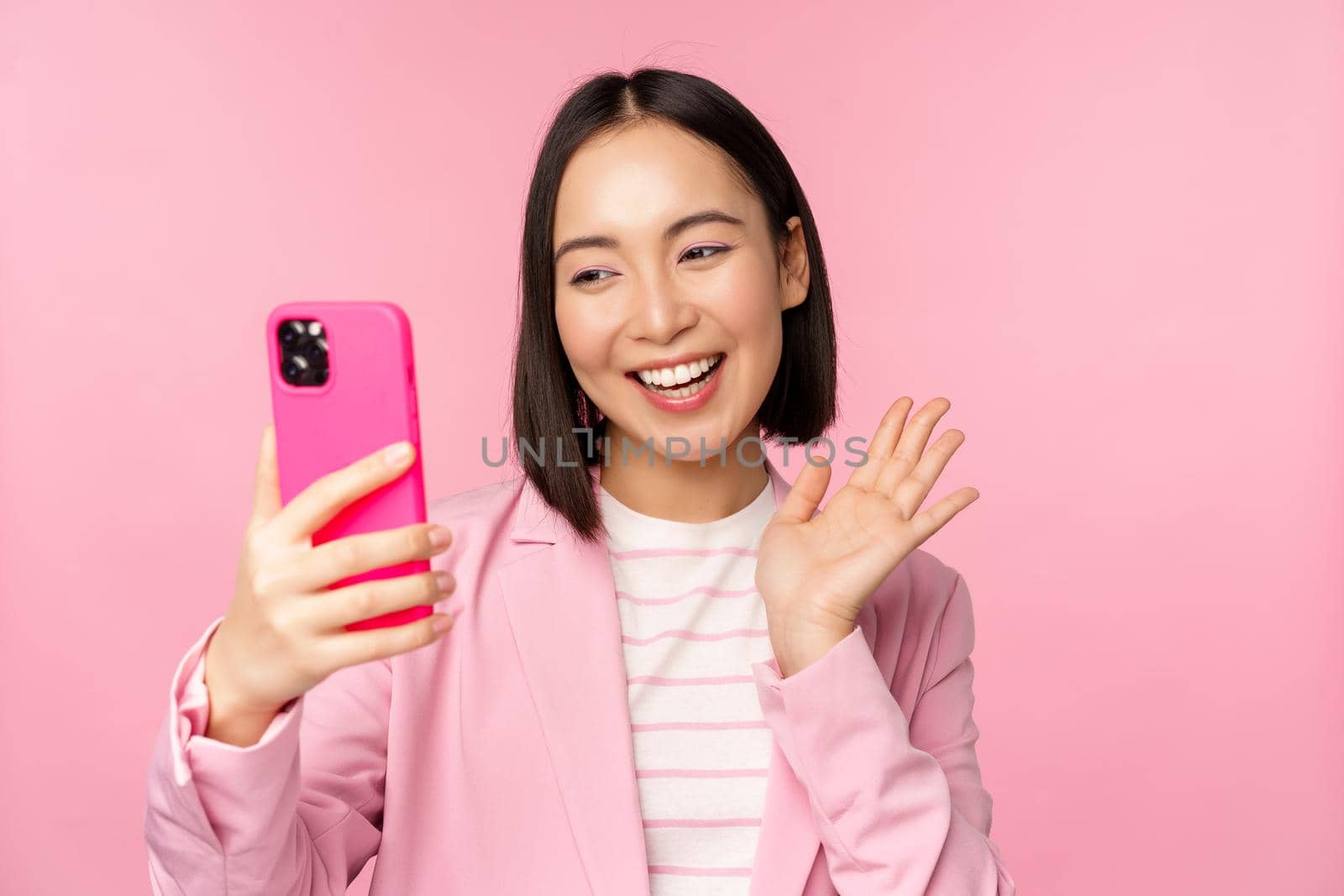 Stylish asian businesswoman, girl in suit taking selfie on smartphone, video chat with mobile phone app, posing against pink studio background by Benzoix