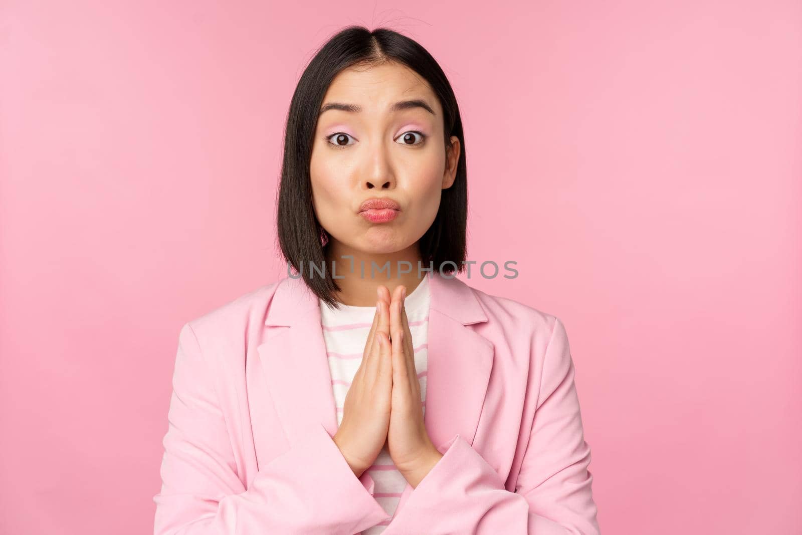 Portrait of asian businesswoman asking for help, say please, standing in praying, begging pose, pink studio background by Benzoix