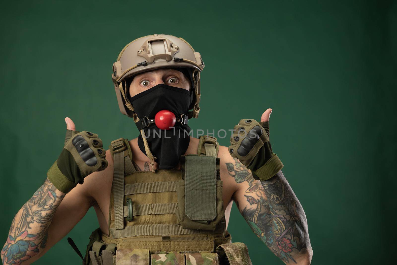 a soldier man in military clothes helmet with a bdsm gag in his mouth expresses emotions, photo joke by Rotozey