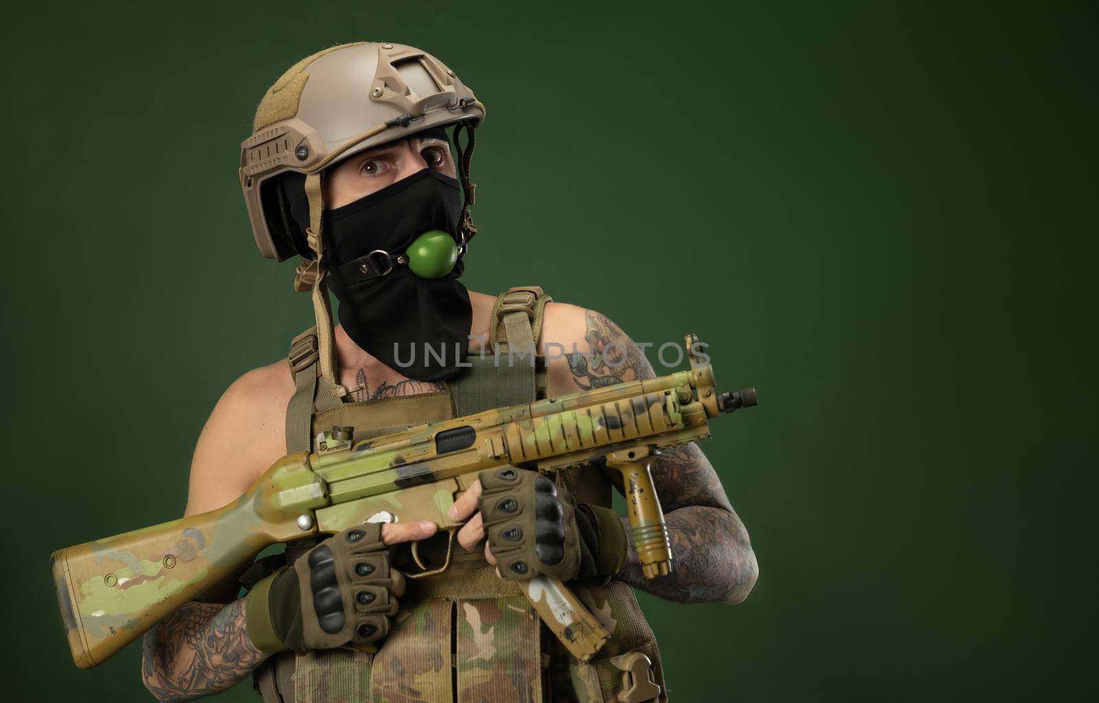 a male soldier in military clothes, a helmet with a bdsm gag in his mouth expresses emotions holding an automatic rifle in his hands, photo joke by Rotozey