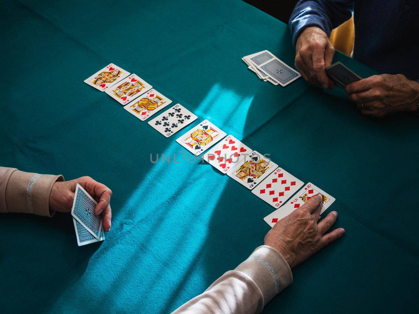 Old men playing a game of cards at home on a green mat. They are in the living room playing cards in natural light. Next to a window, zenithal photo.