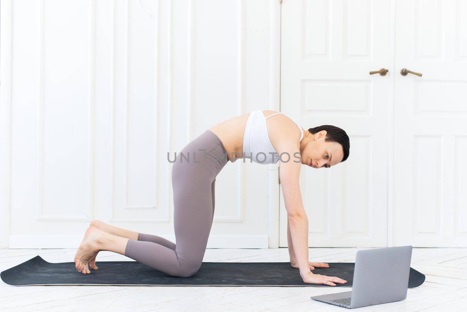 A sporty woman in sportswear is sitting on the floor and is using a laptop at home in the living room. Sport and recreation concept.