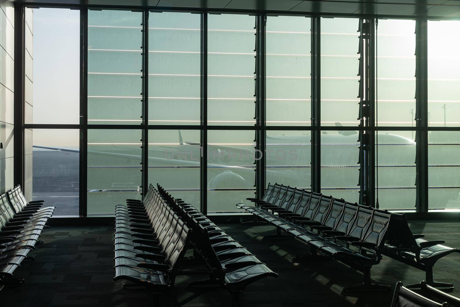 a deserted airport, empty benches by a panoramic window, a huge plane visible through the glass walls of an interchange hub in the United Arab Emirates. High quality photo