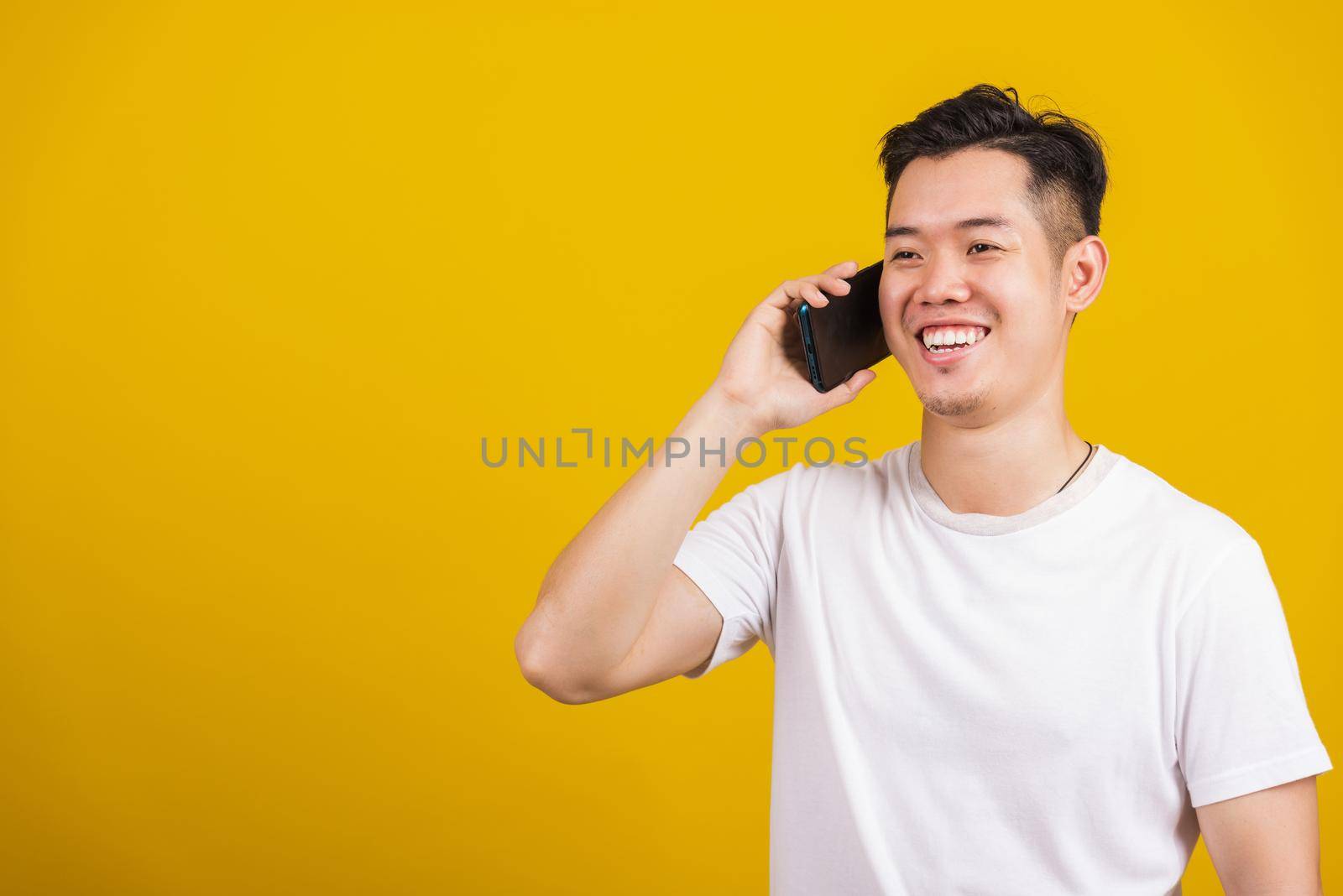 Asian handsome young man smiling positive talking on cellphone, lifestyle happy male using mobile smartphone studio shot isolated on yellow background