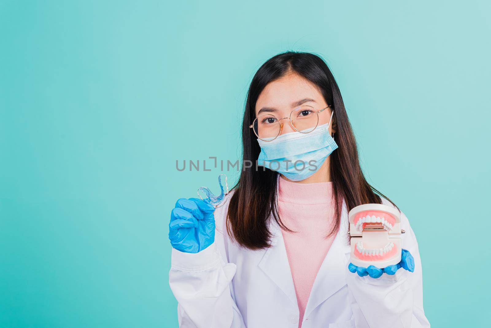 Asian beautiful woman dentist holding silicone orthodontic retainers and model teeth denture isolated on blue background, Teeth retaining tools after removable braces, Orthodontics dental healthy care