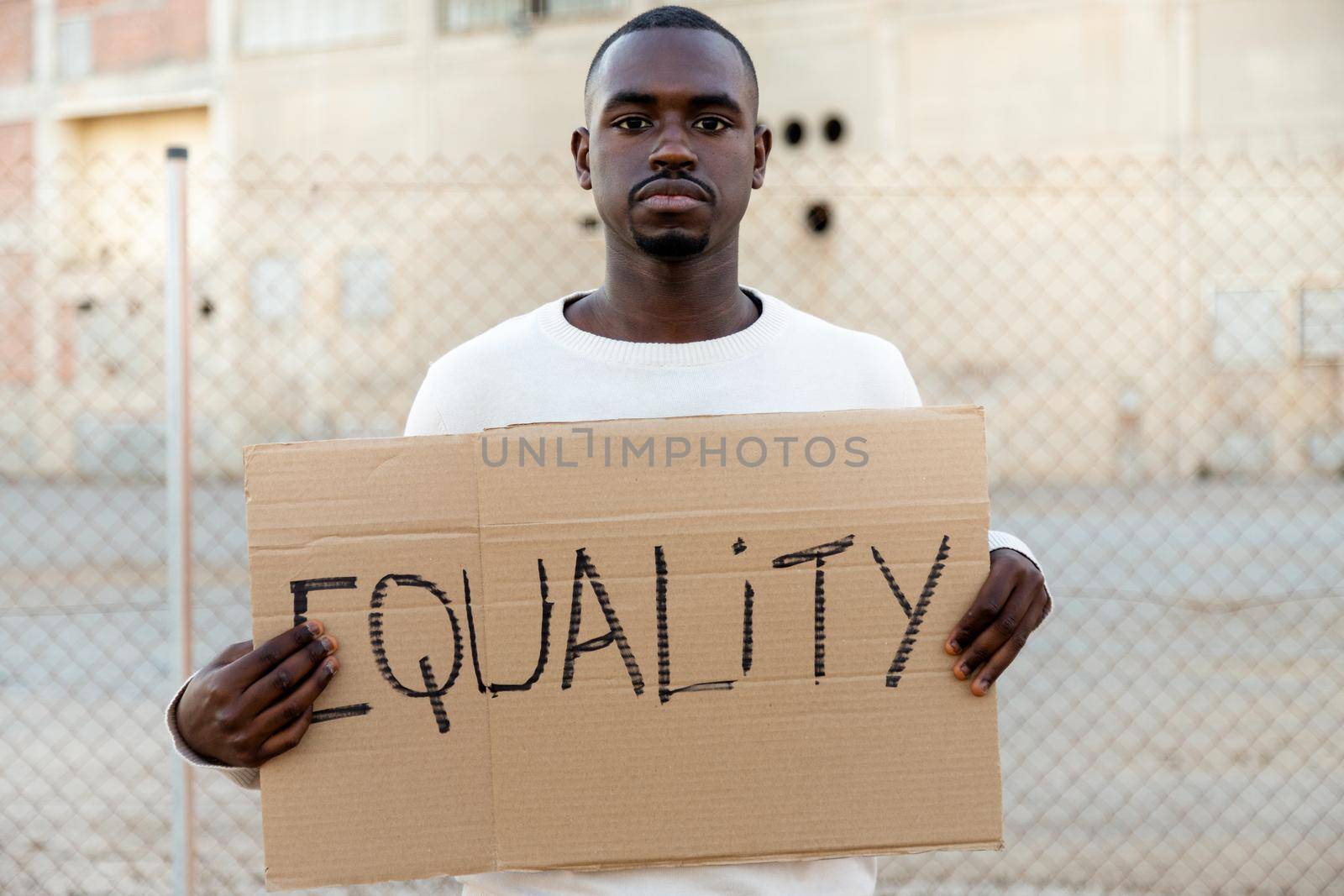 Young African American man looking at camera holding cardboard sign: Equality. Human rights activist. by Hoverstock