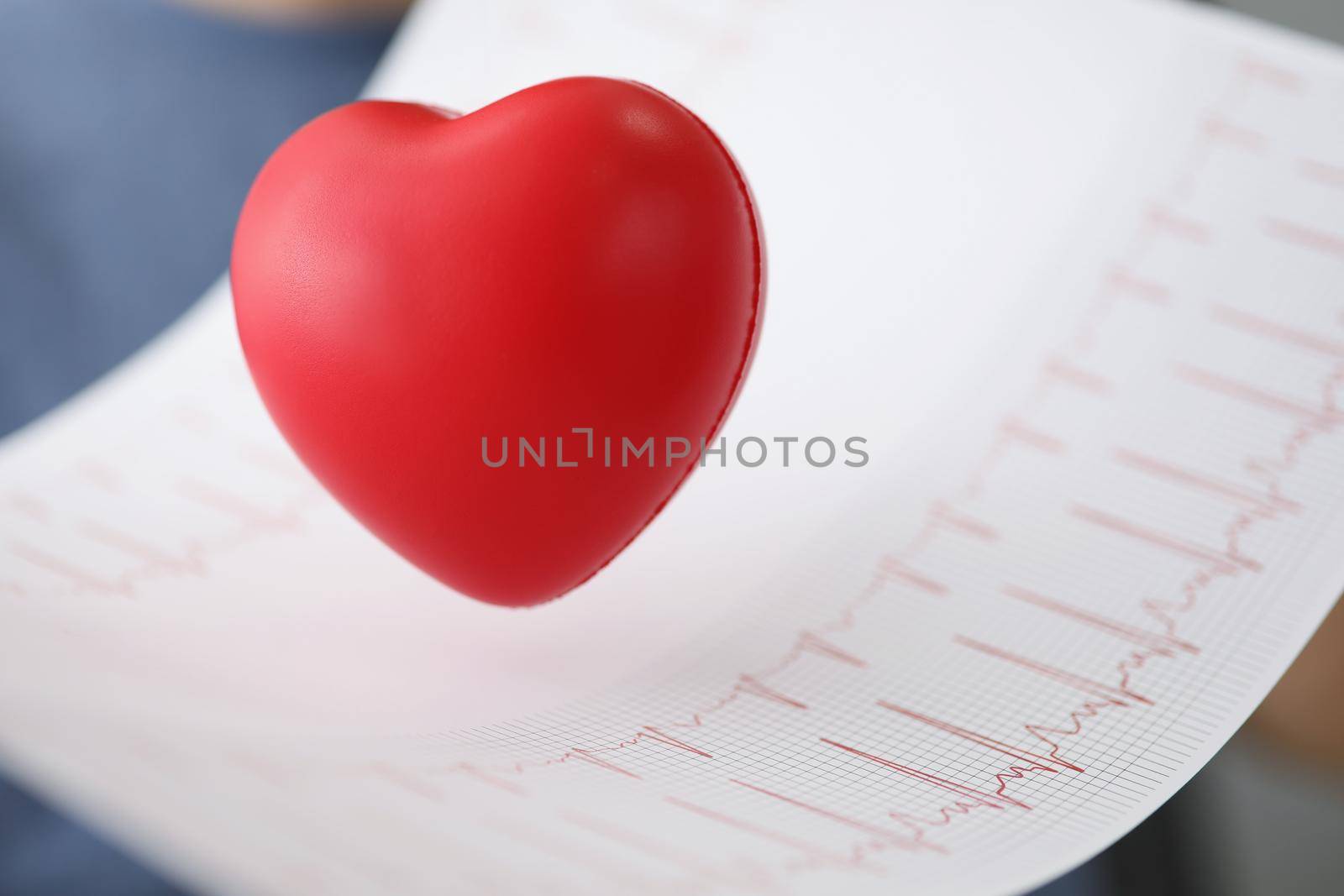 Close-up of red plastic heart with electrogram result, professional diagnostic. Planned checkup at clinic, heart analysis. Ecg, cardiology, health concept