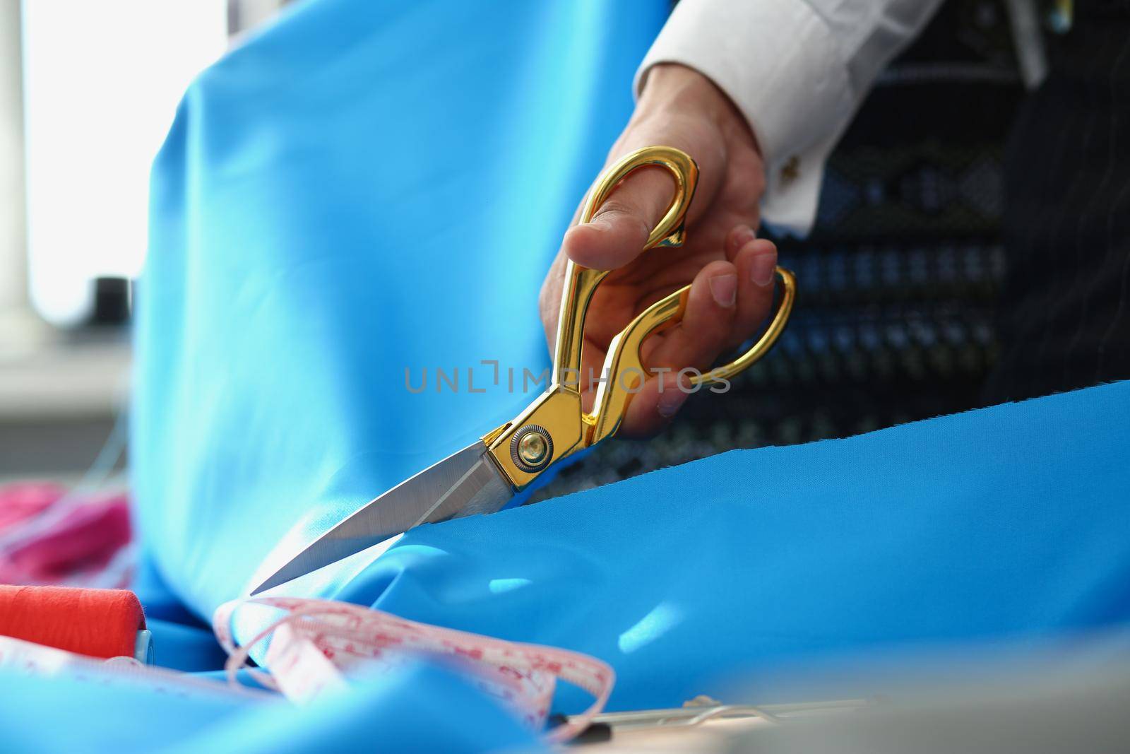 Close-up of person cutting blue cotton cloth with scissors tool for further sewing. Creative process at cloth studio, idea. Fashion, atelier, art concept